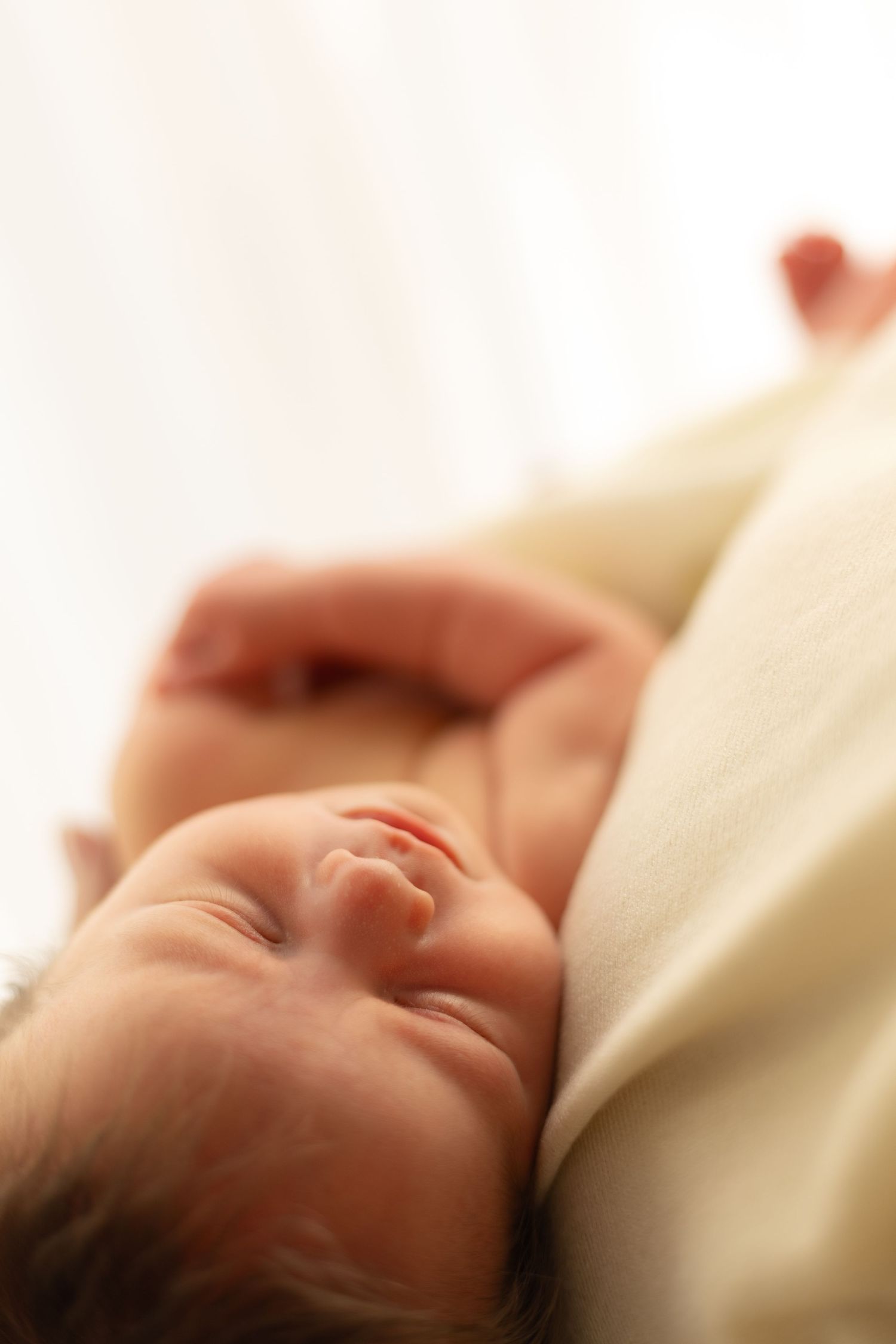 A peaceful sleeping baby lies swaddled in soft cream-colored bedding.