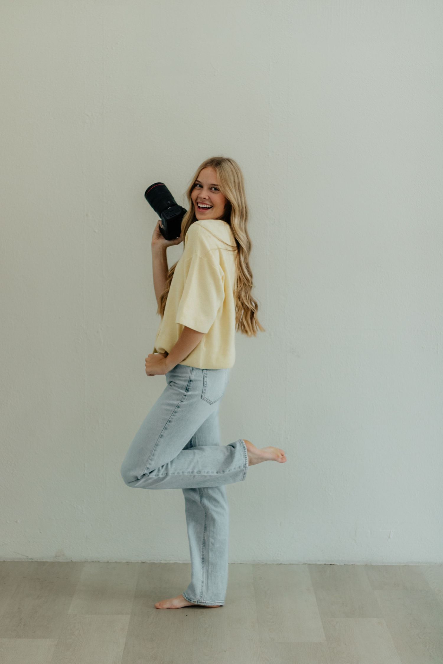 Woman in light yellow top and baggy jeans dances playfully against white wall in four sequential poses.