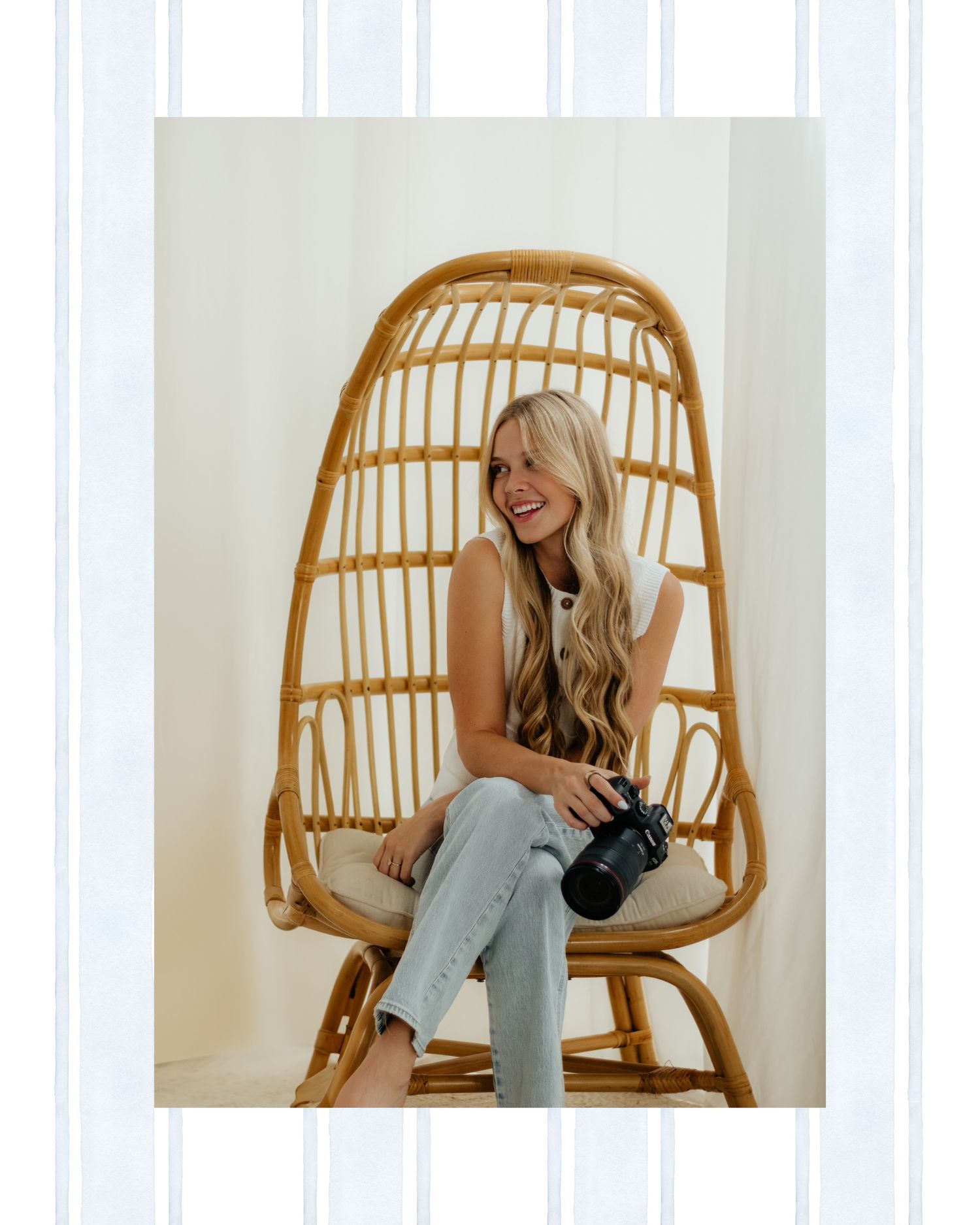 Smiling blonde woman holding a camera sits in a rattan egg chair against a white background.