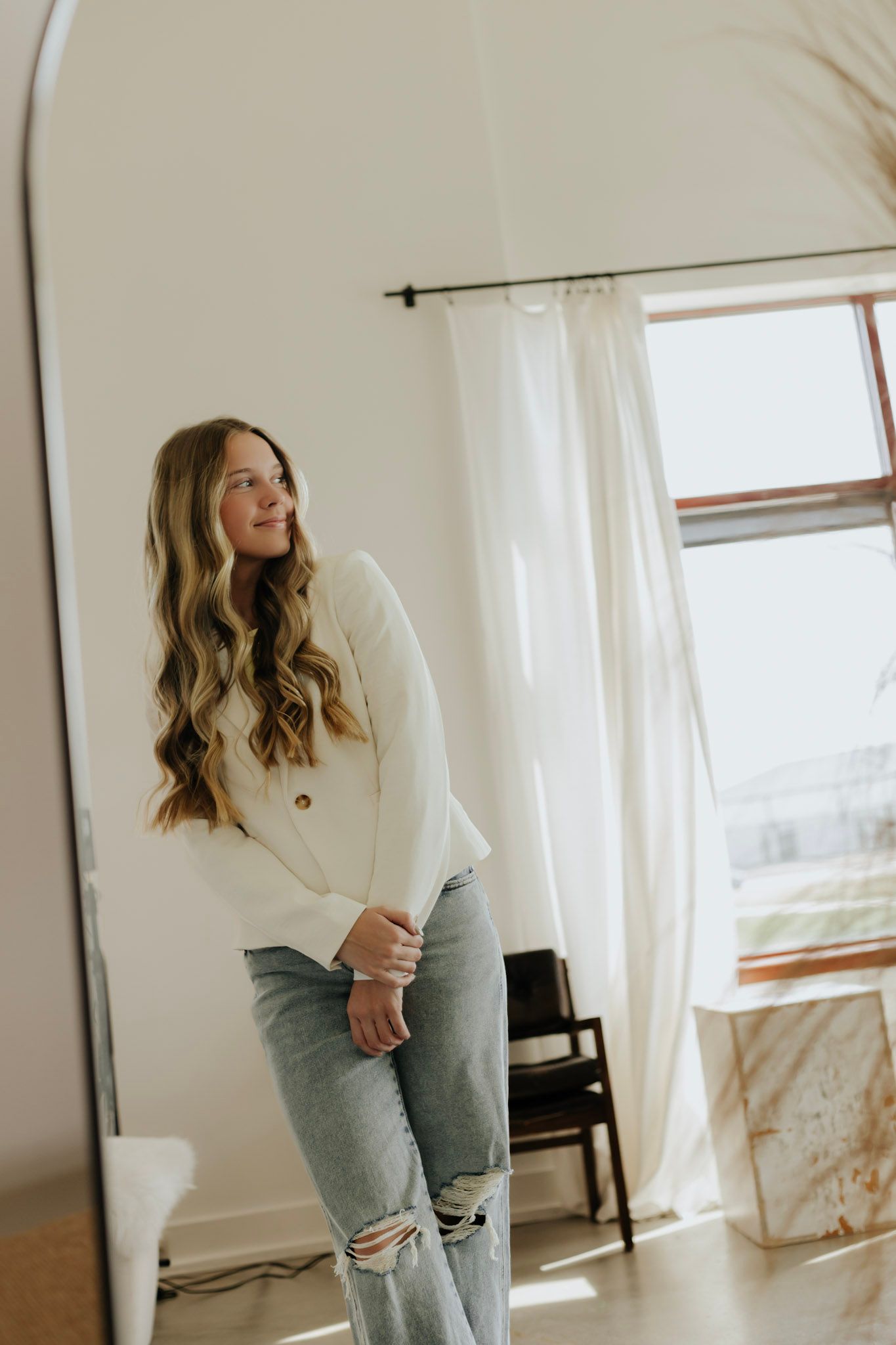 Fashion portrait of woman in white sweater and distressed jeans by bright window.
