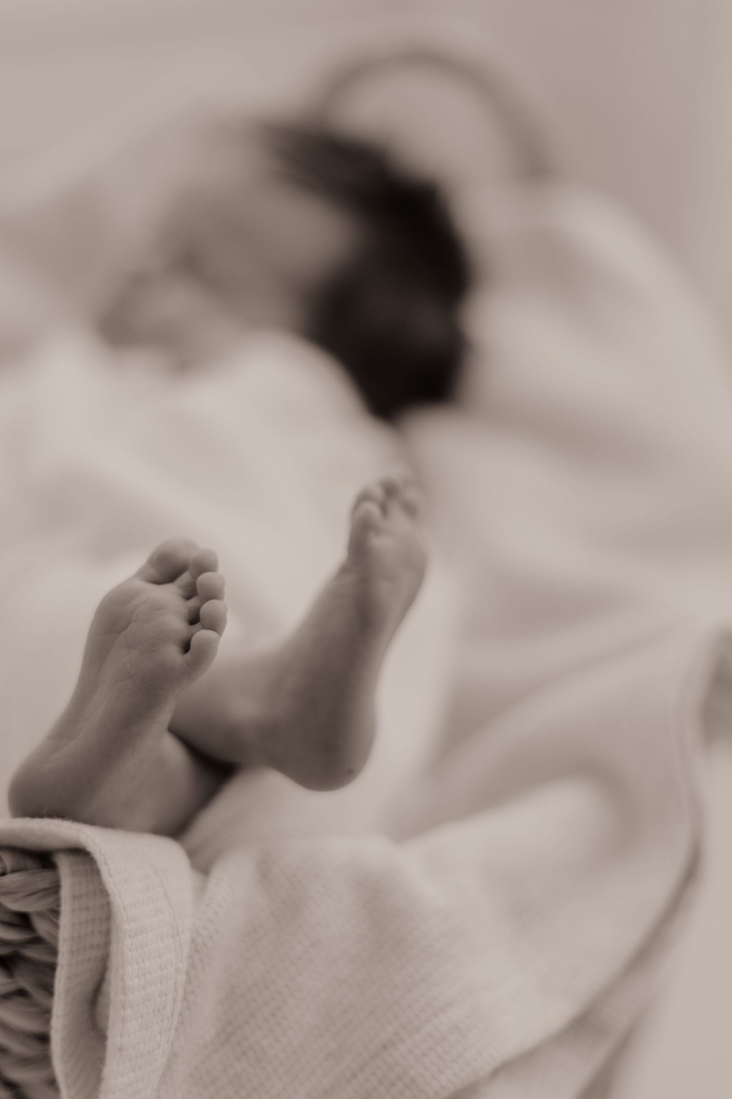 A black and white close-up photograph of tiny baby feet wrapped in soft white blankets.
