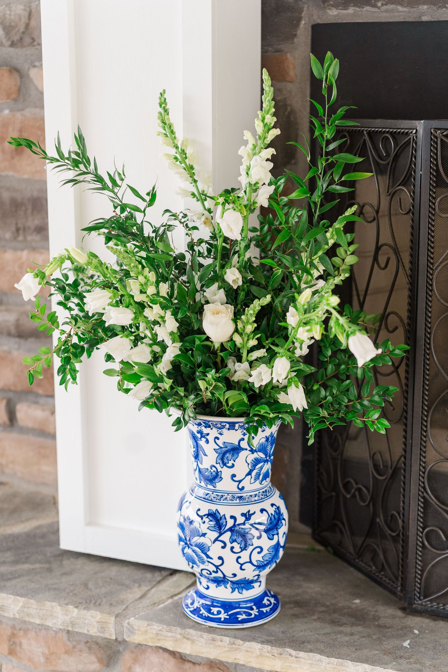 White floral arrangement with delicate blooms and greenery displayed in a traditional blue and white chinoiserie vase on a ledge.