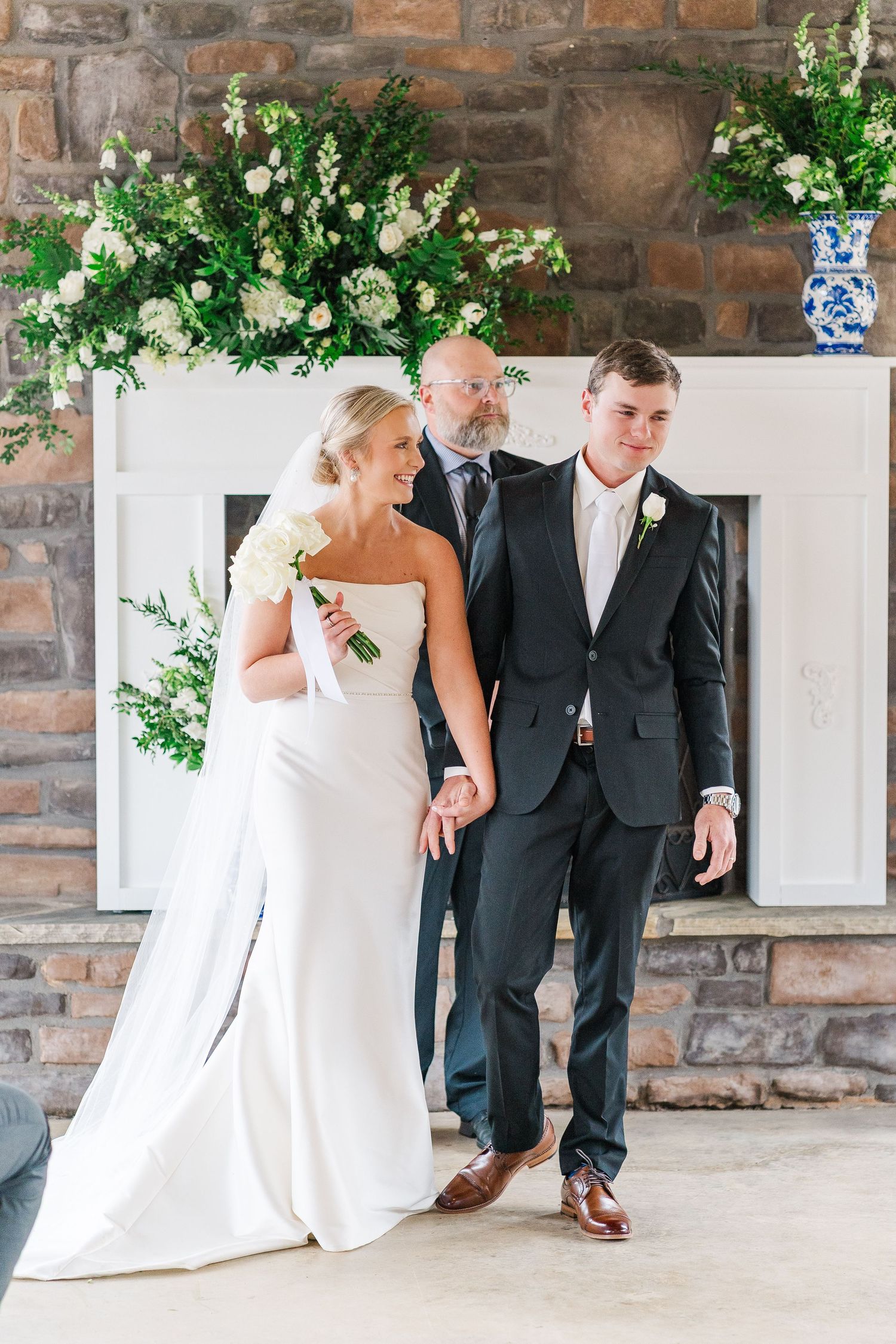 Elegant wedding ceremony in stone venue with white floral arrangements and decor against rustic brick wall.