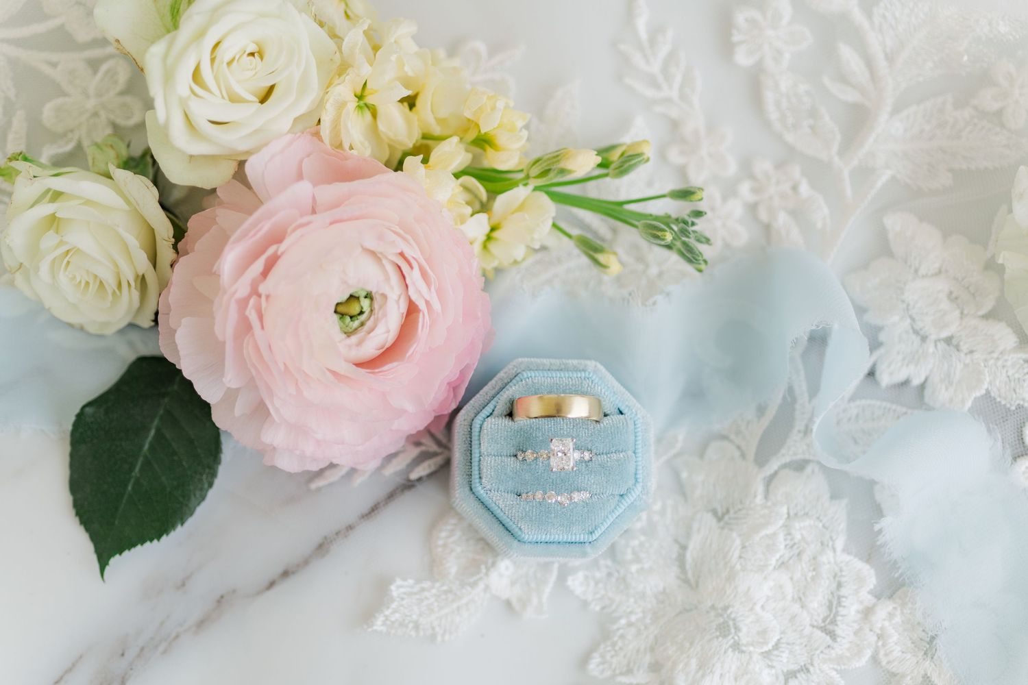 Pink and white ranunculus flowers with delicate lace and blue accents create a romantic wedding styled flatlay.