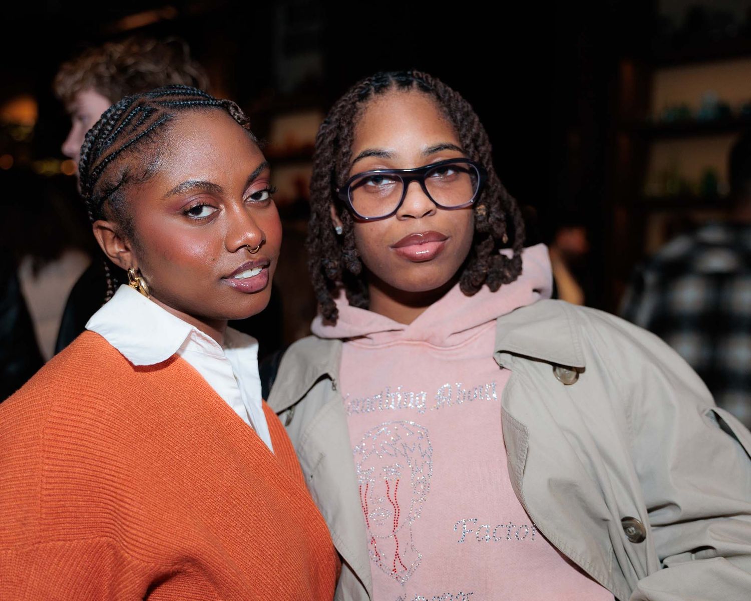 Two people pose together wearing contrasting outfits in orange and pink at a social event.