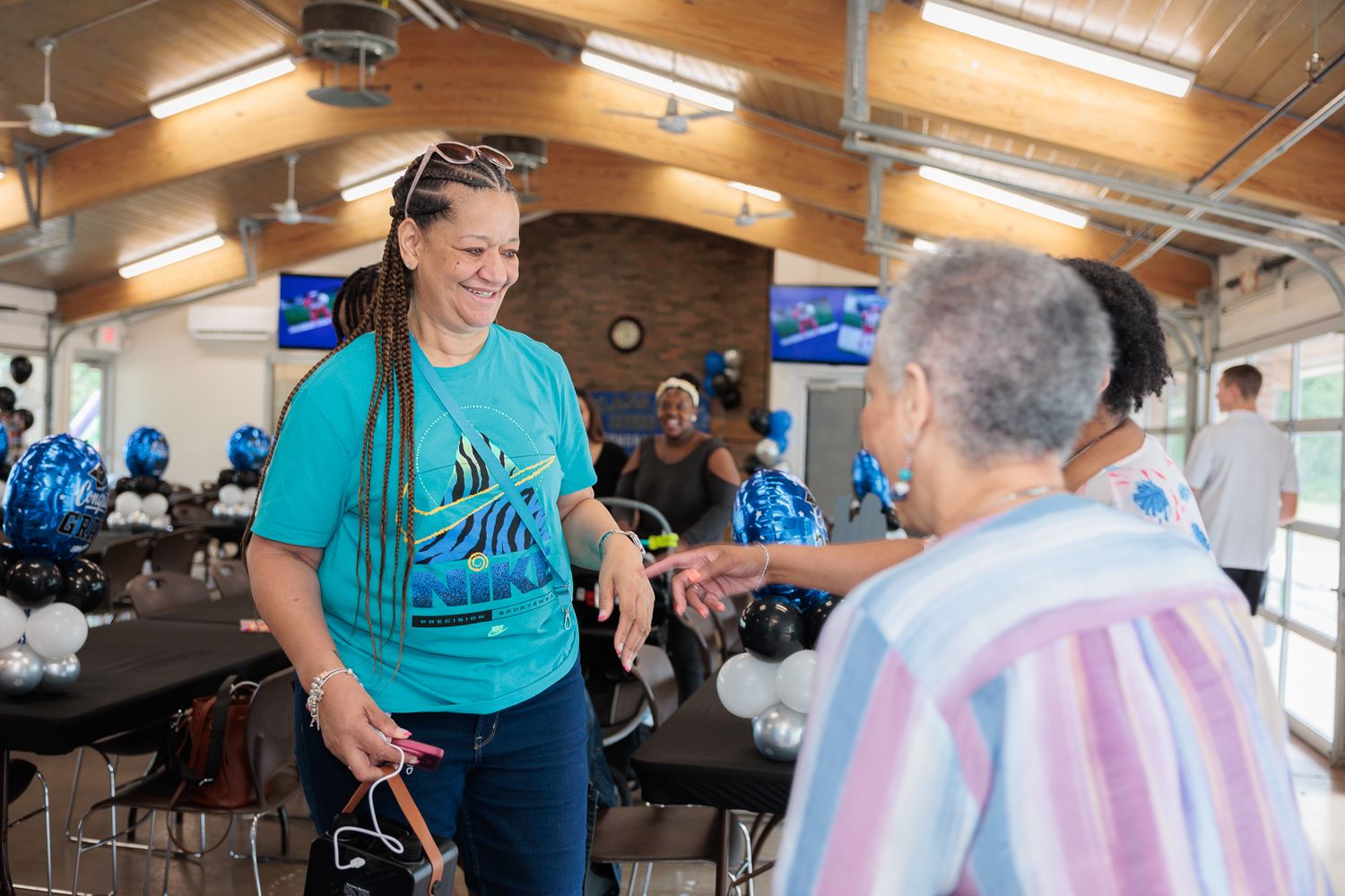 Two women greeting each other at a festive indoor event with blue and black balloon decorations.