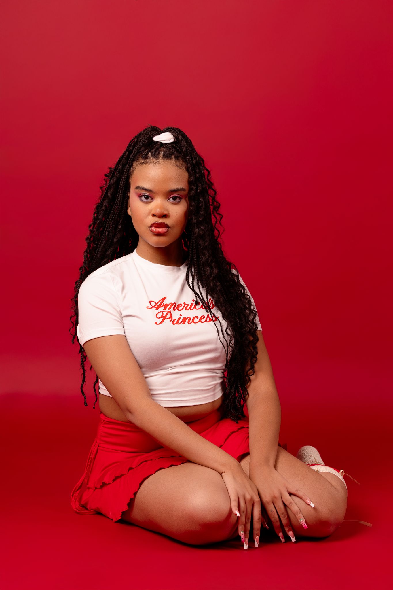 A person in a white crop top poses expressively against a vibrant red backdrop in a fashion photo series.