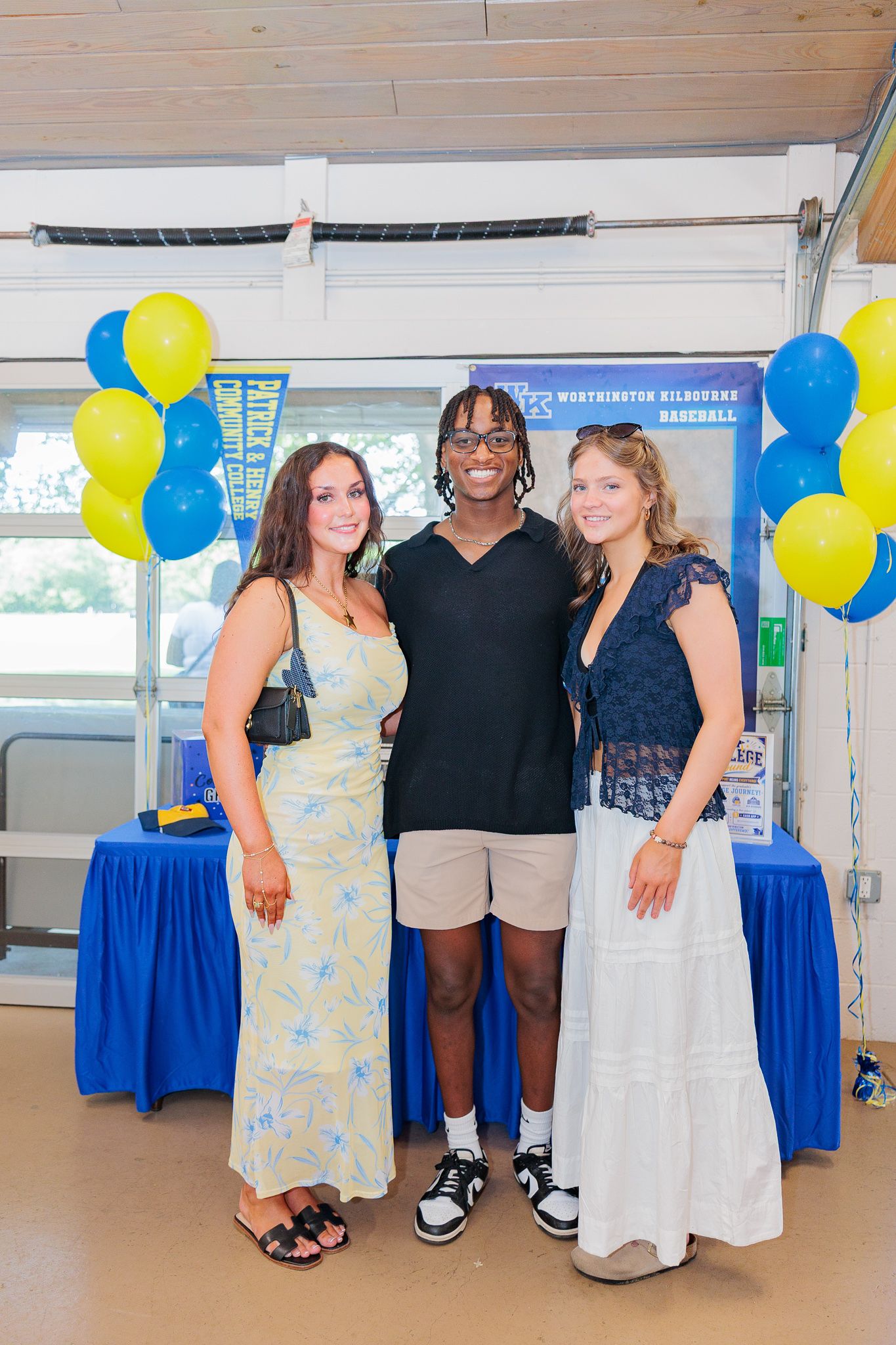 Three teens pose together at a Worthington Kilbourne Baseball celebration with blue and yellow balloons.
