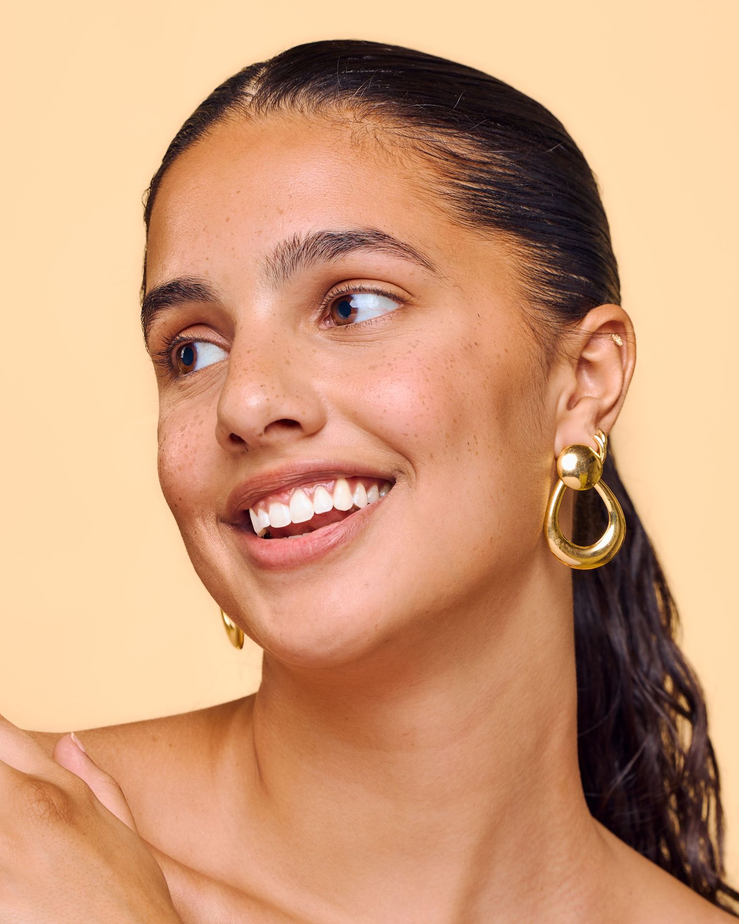 Beautiful smile and gold hoop earrings against a peach background in a beauty portrait.