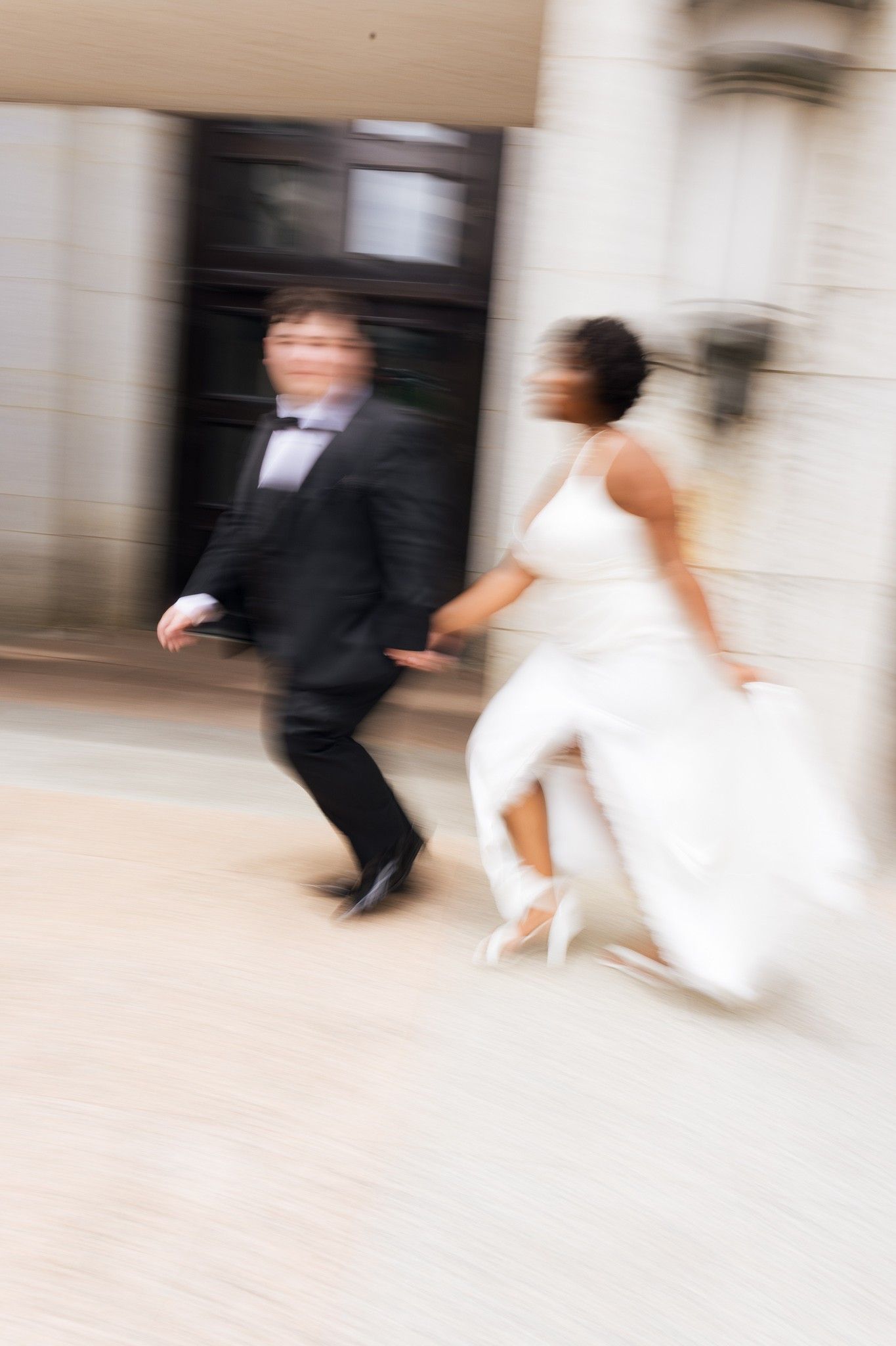 Motion blur photo of interracial bride and groom running together on wedding day.