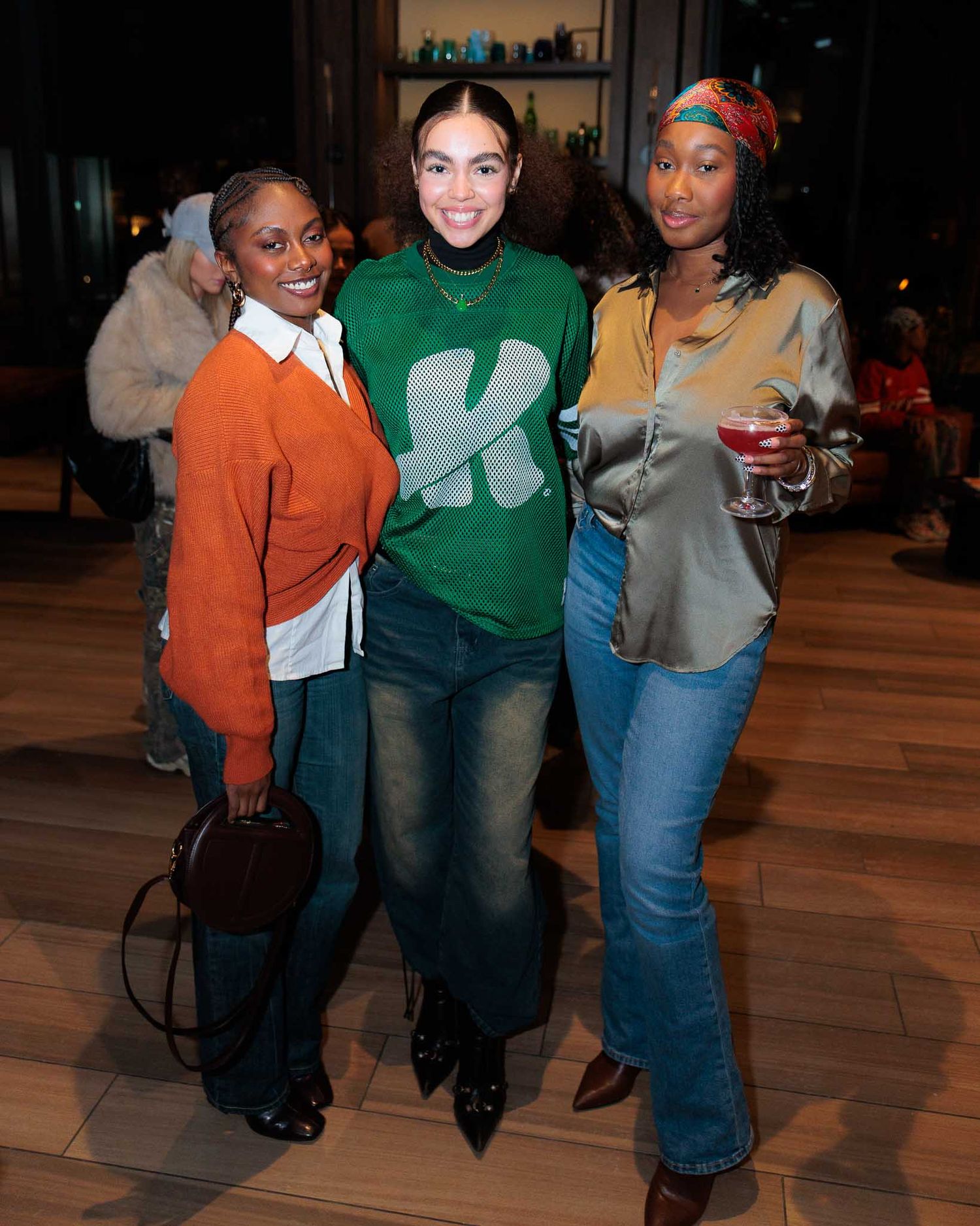 Three friends pose together in casual outfits at an indoor venue during a social gathering.
