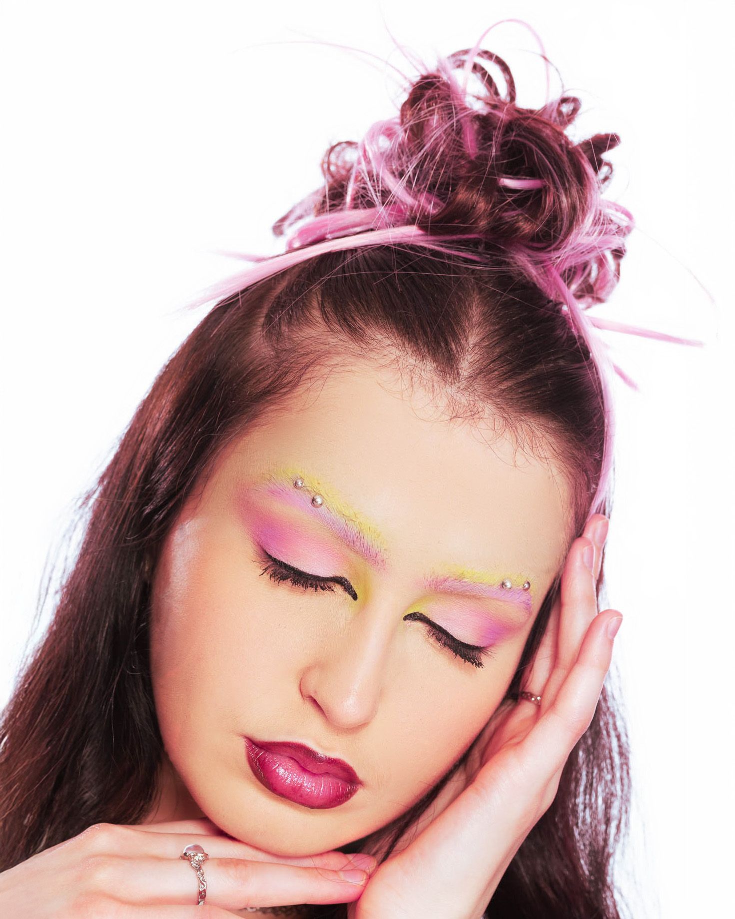 Creative beauty portrait with pink hairstyle, bold lip color and artistic glitter eyebrow makeup in soft lighting.