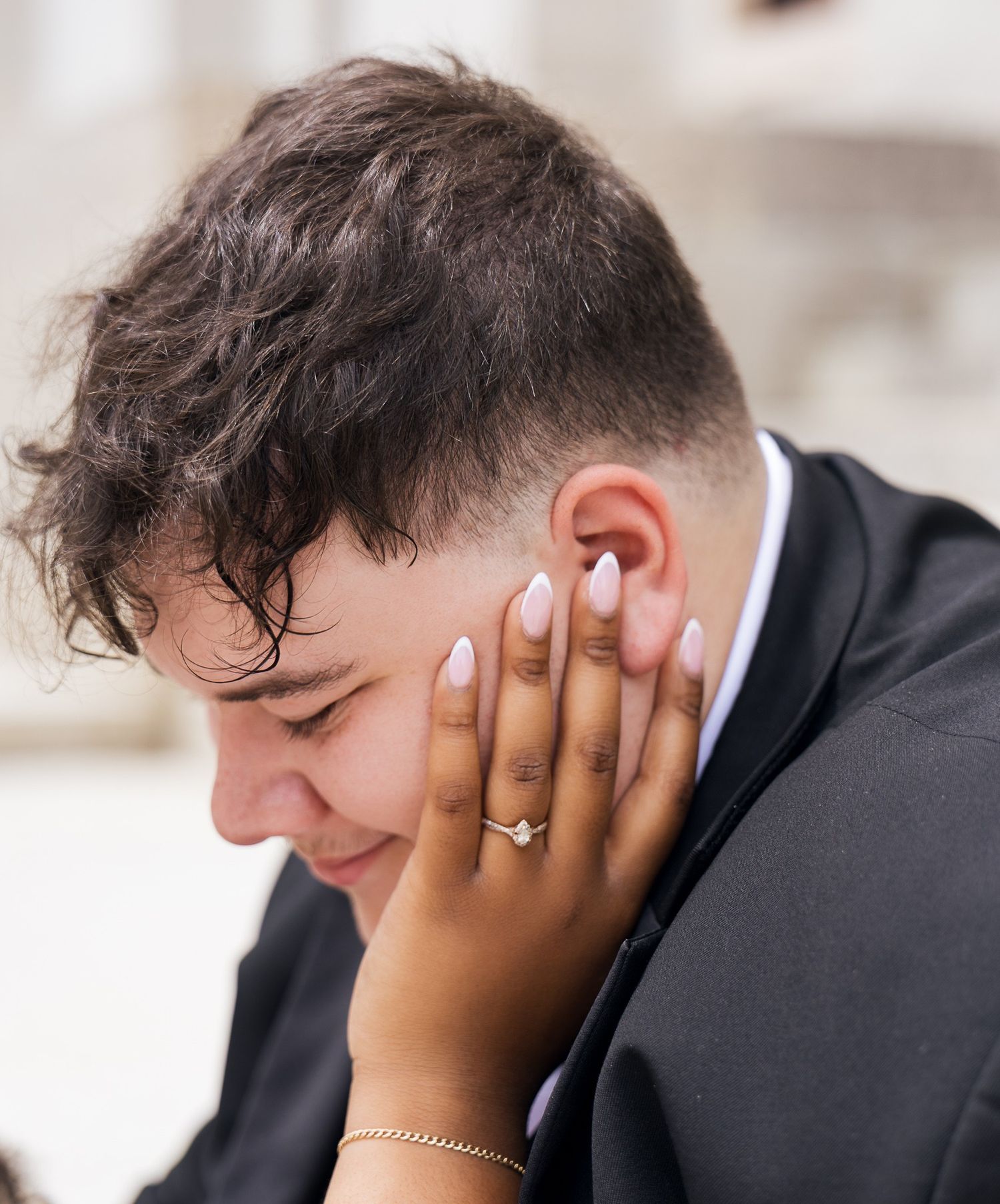 Close-up of a bride's hand with engagement ring and bracelet gently touching groom's face at their wedding.