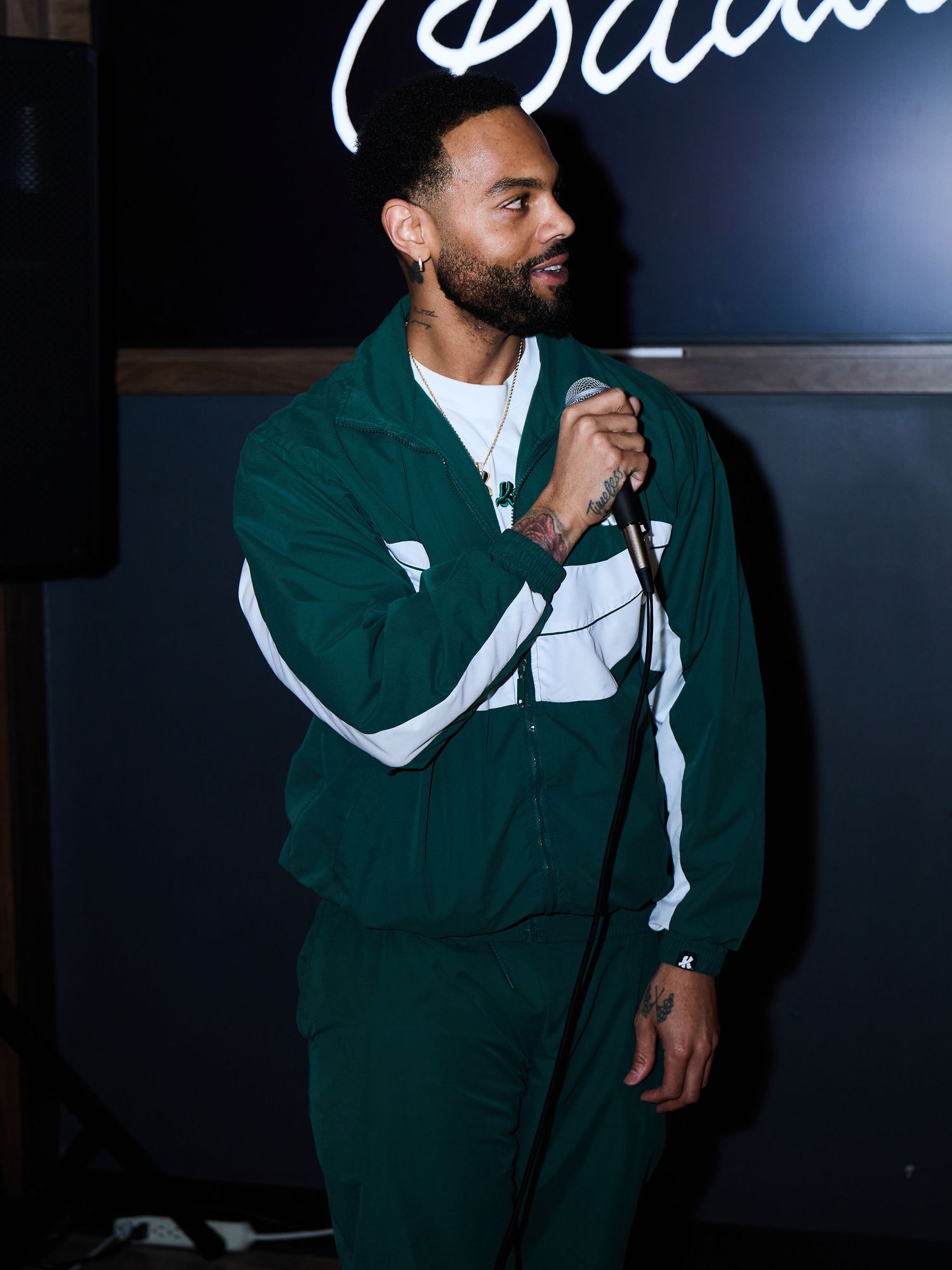 A person wearing a dark green and white varsity jacket poses against a black background.