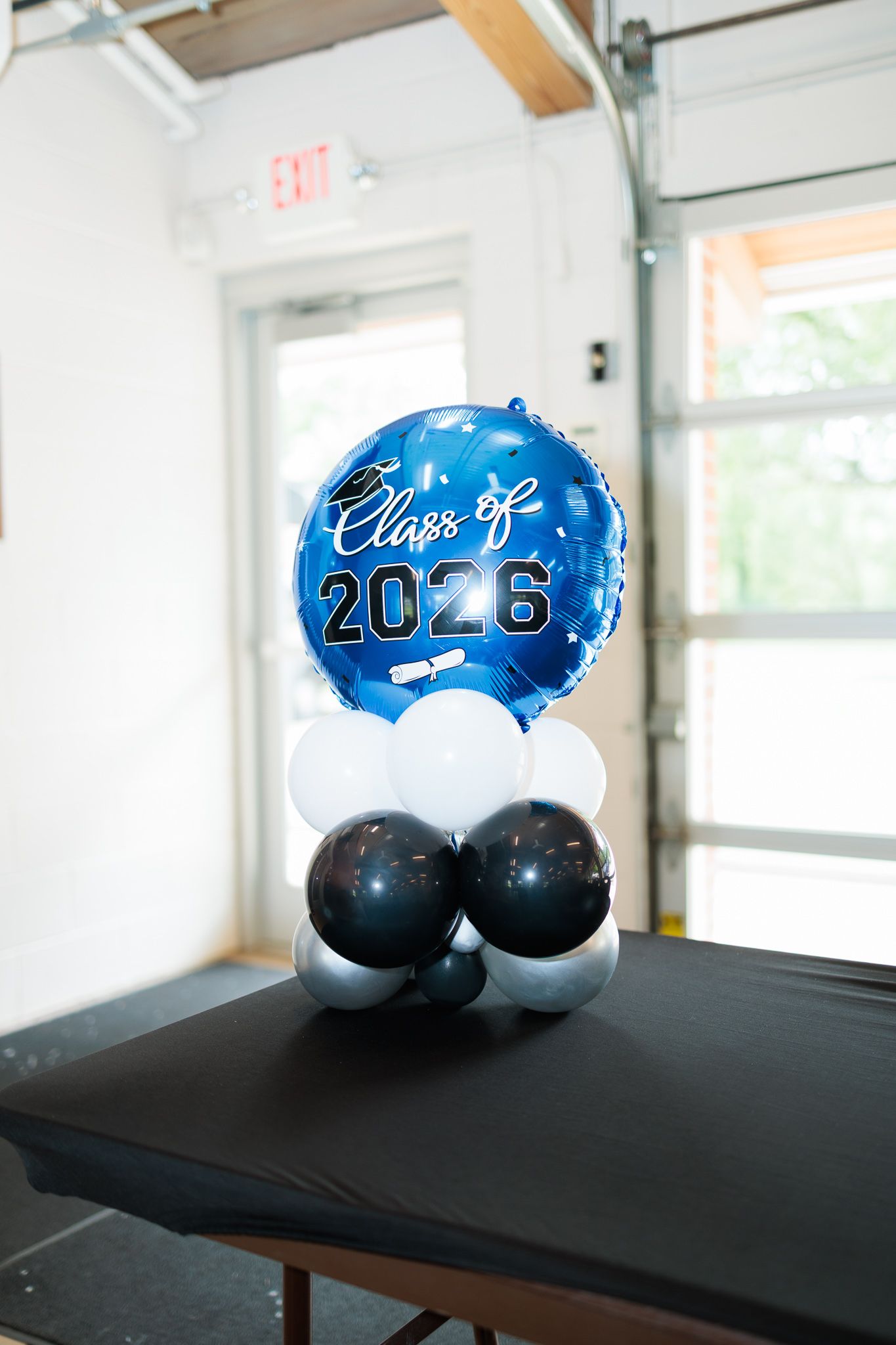 Class of 2026 graduation balloon centerpiece in blue, black, and white on a table.
