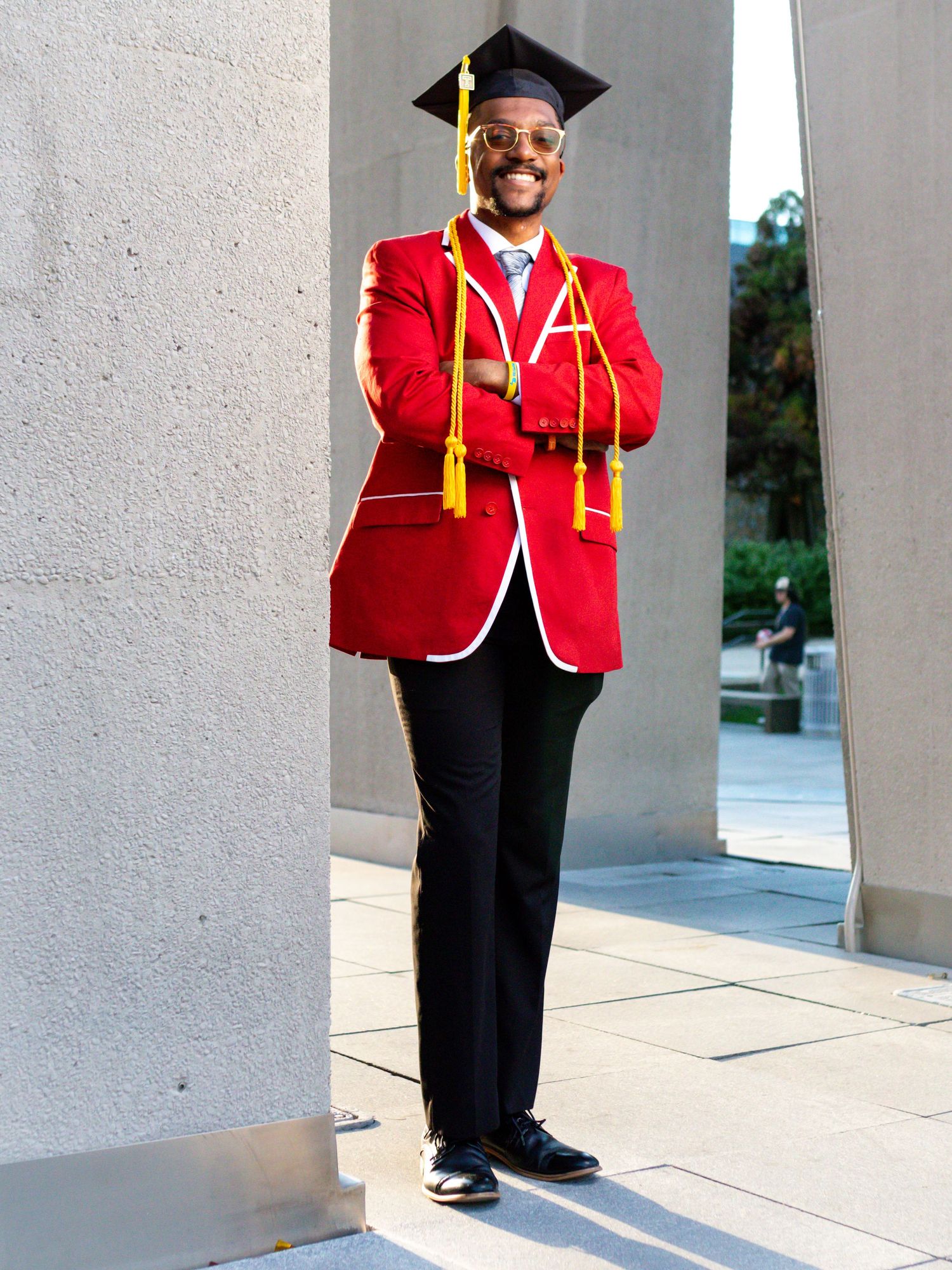 Graduate in vibrant red blazer and cap stands between architectural columns.
