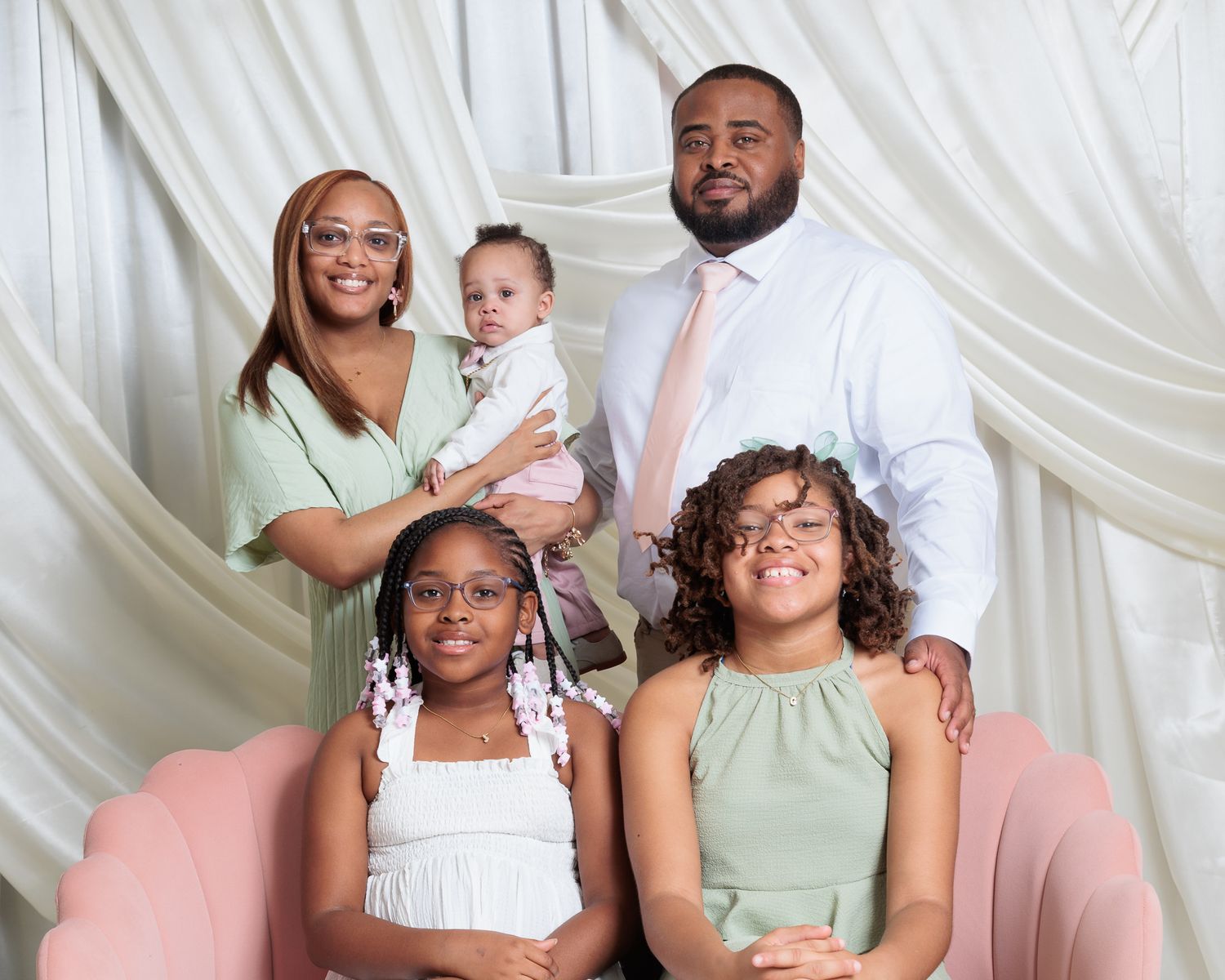 A joyful family of five poses for a professional portrait, with parents and three children dressed in elegant pastel outfits.
