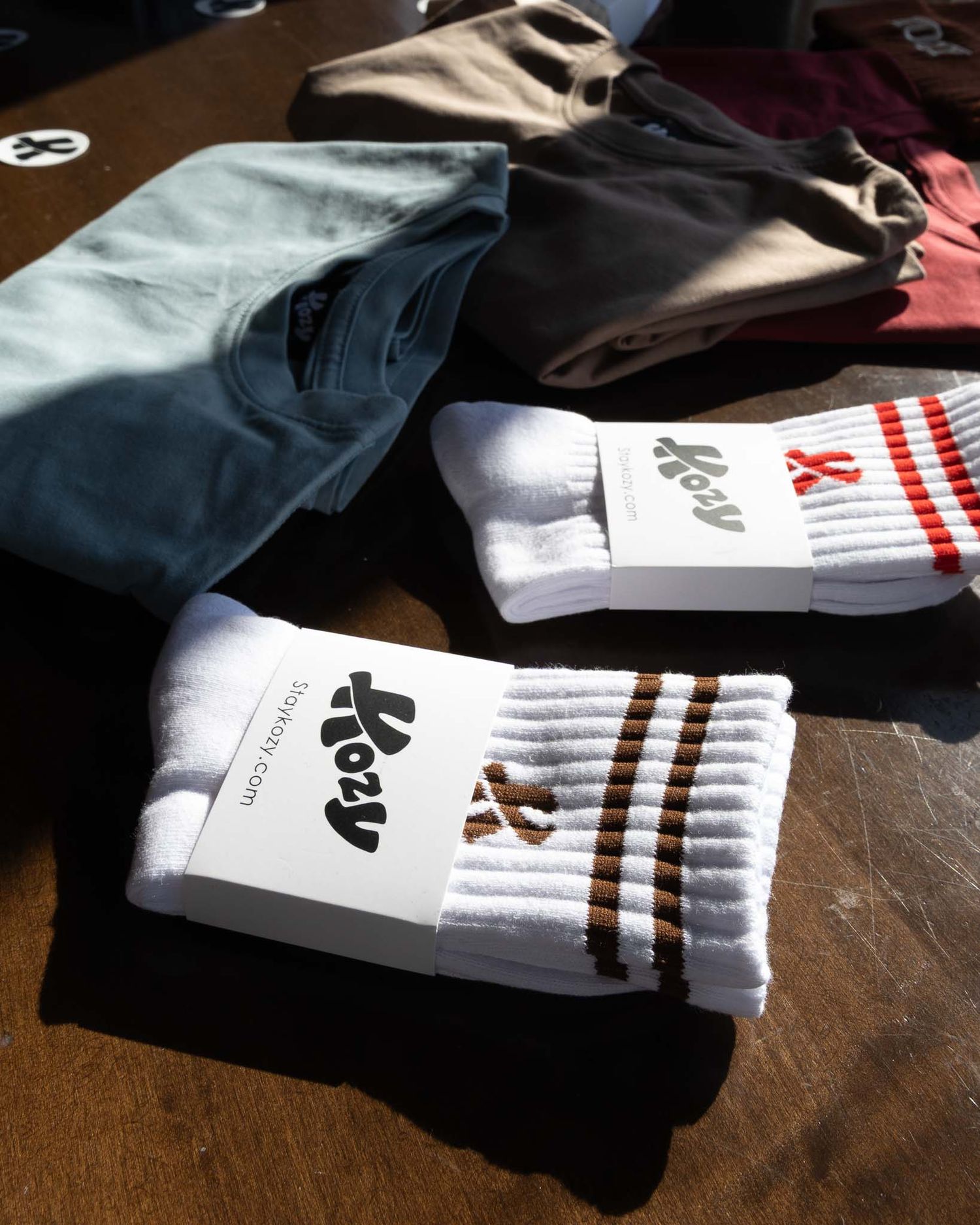 White athletic socks with brown stripes and a logo design displayed on a wooden surface next to folded clothing.