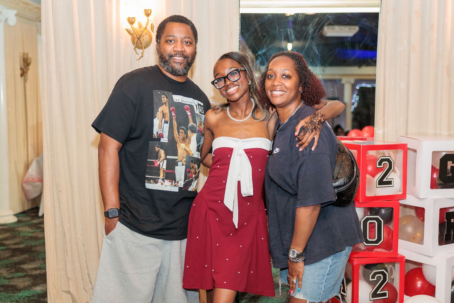 Three people smiling together at a graduation celebration party with decorative 2020 blocks in the background.