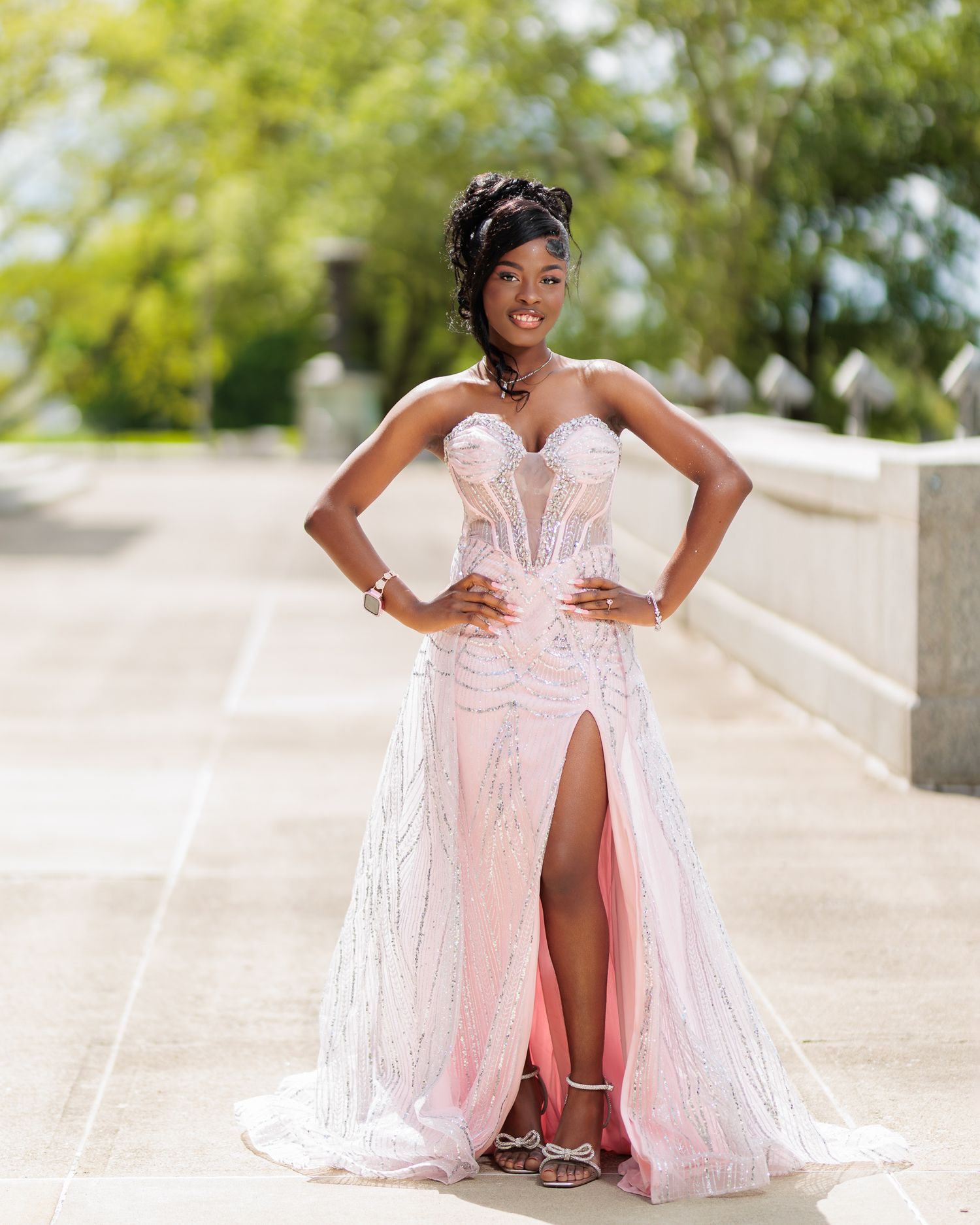 Elegant young woman poses in pink strapless sequin mermaid gown with thigh slit at outdoor venue.