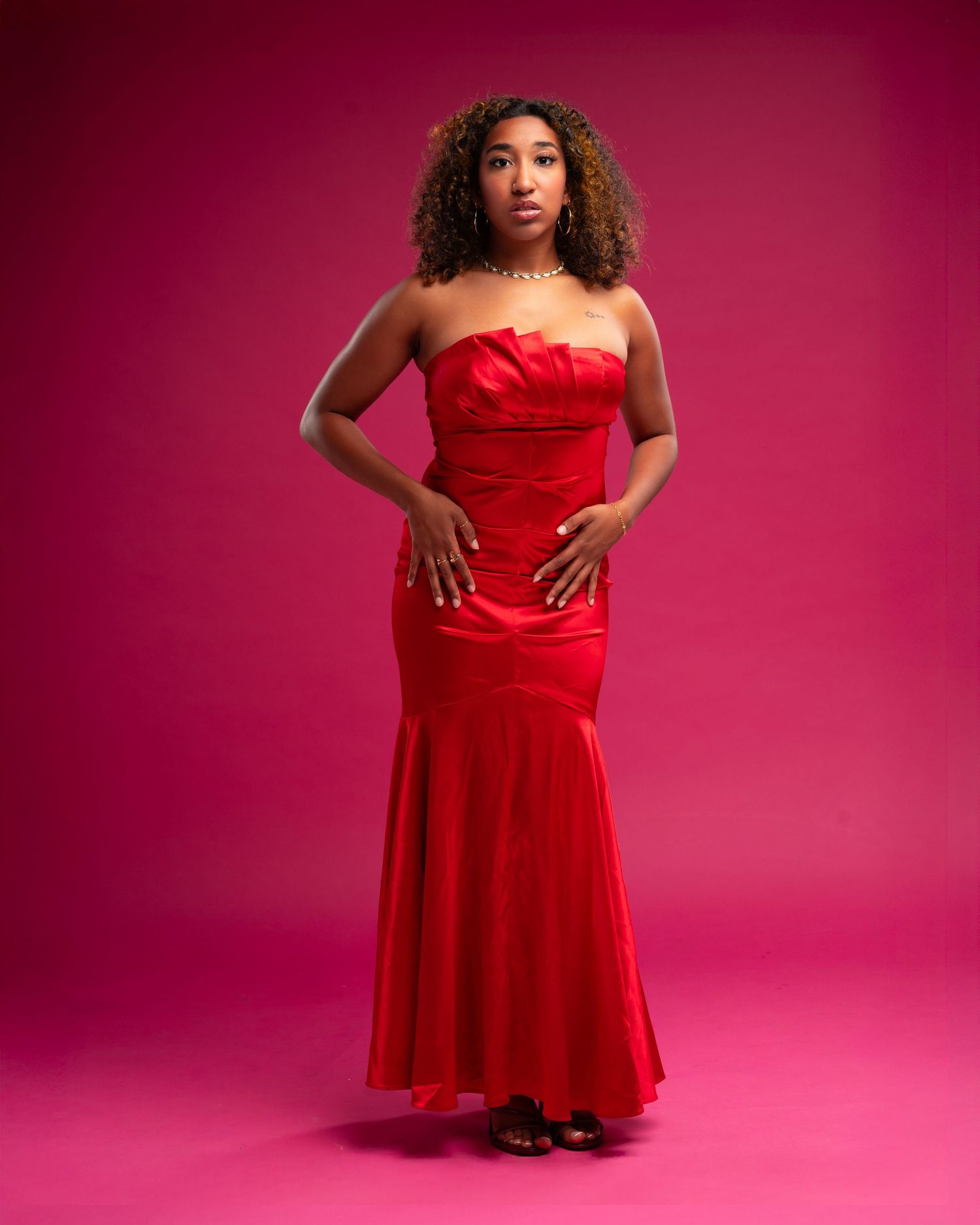 Model in a vibrant red dress poses elegantly against a pink studio backdrop.