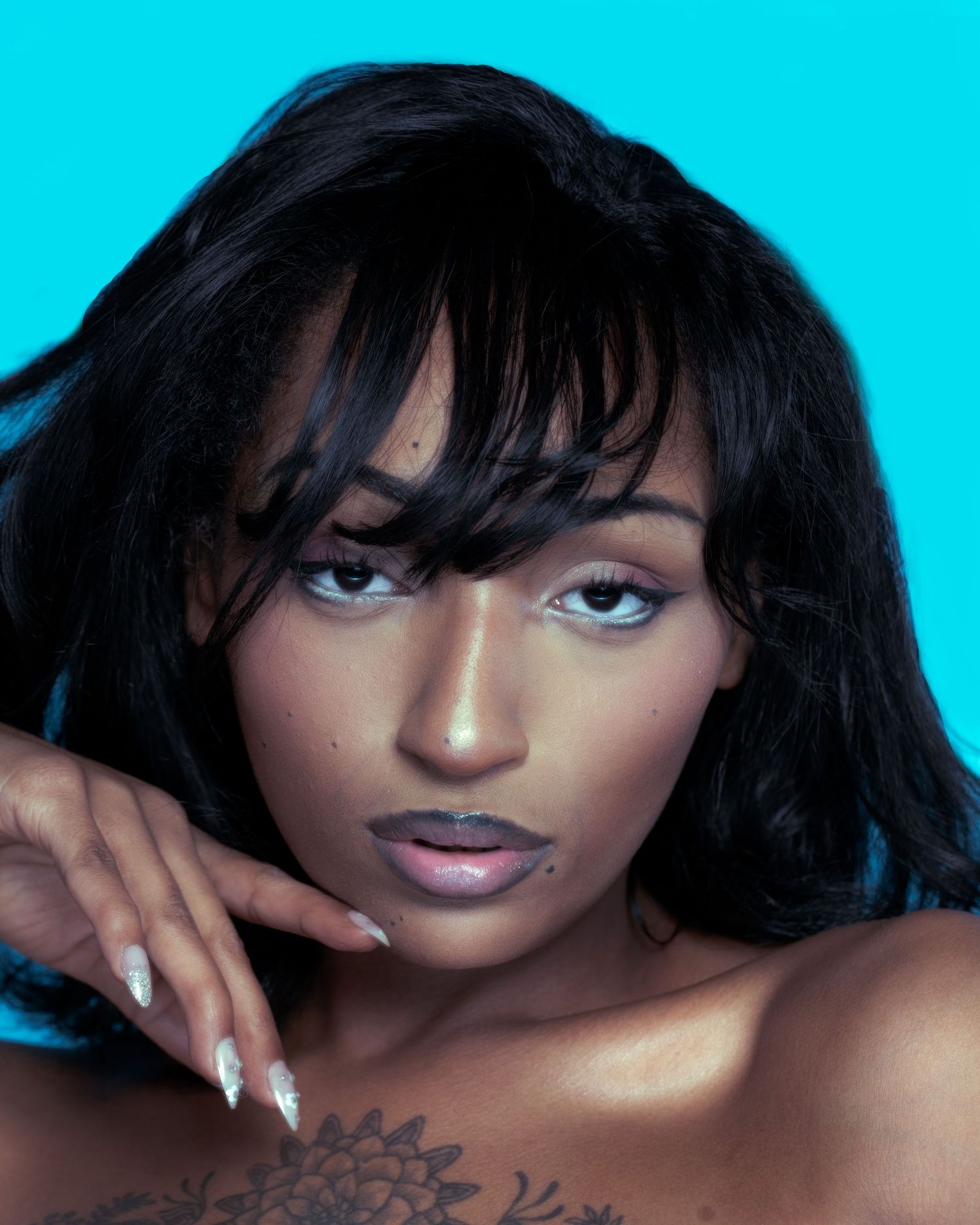 Portrait shot against turquoise background showing glossy black hair, nude shoulders and stylish silver nails.