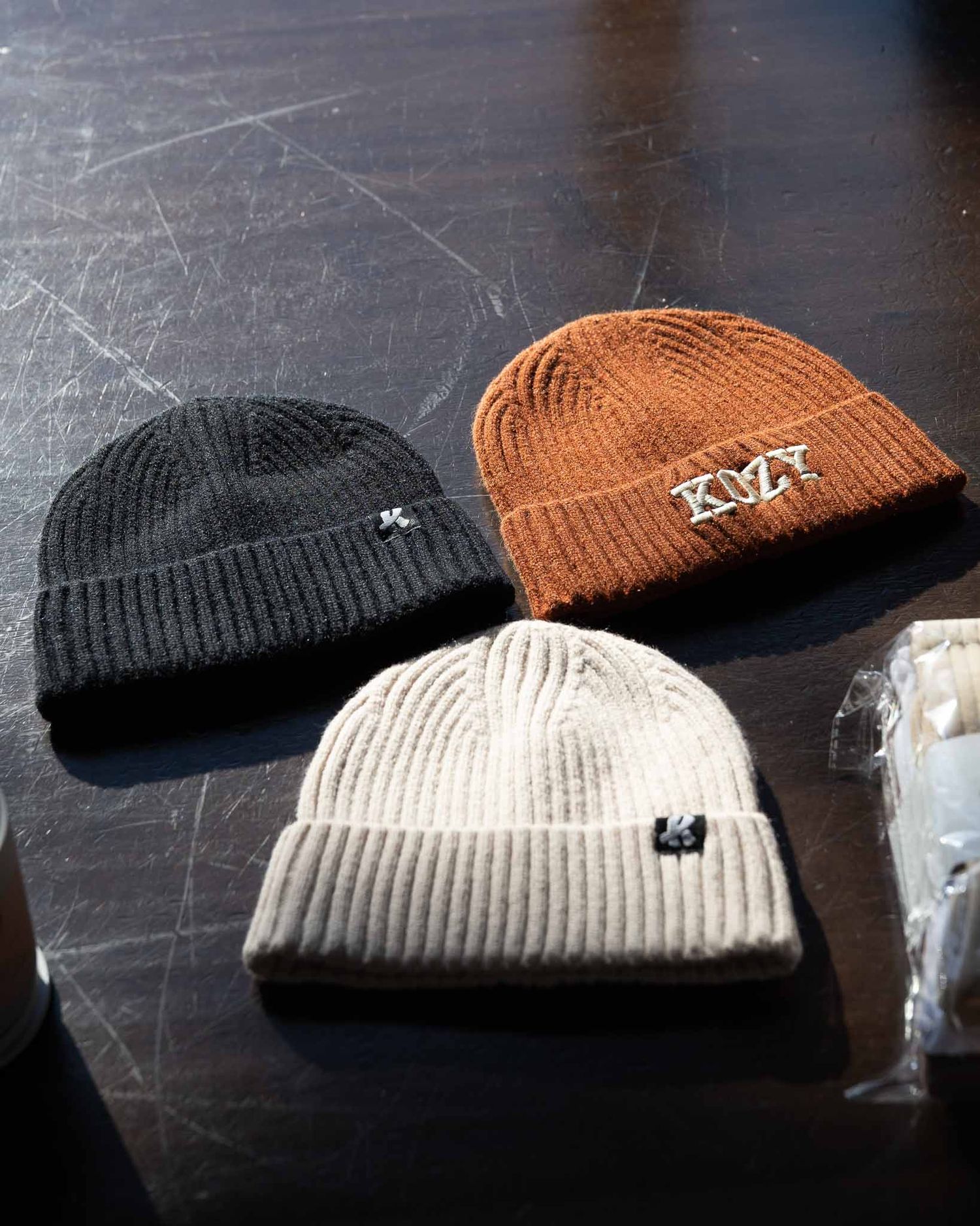Three knit beanies in black, beige, and orange arranged on a dark surface.