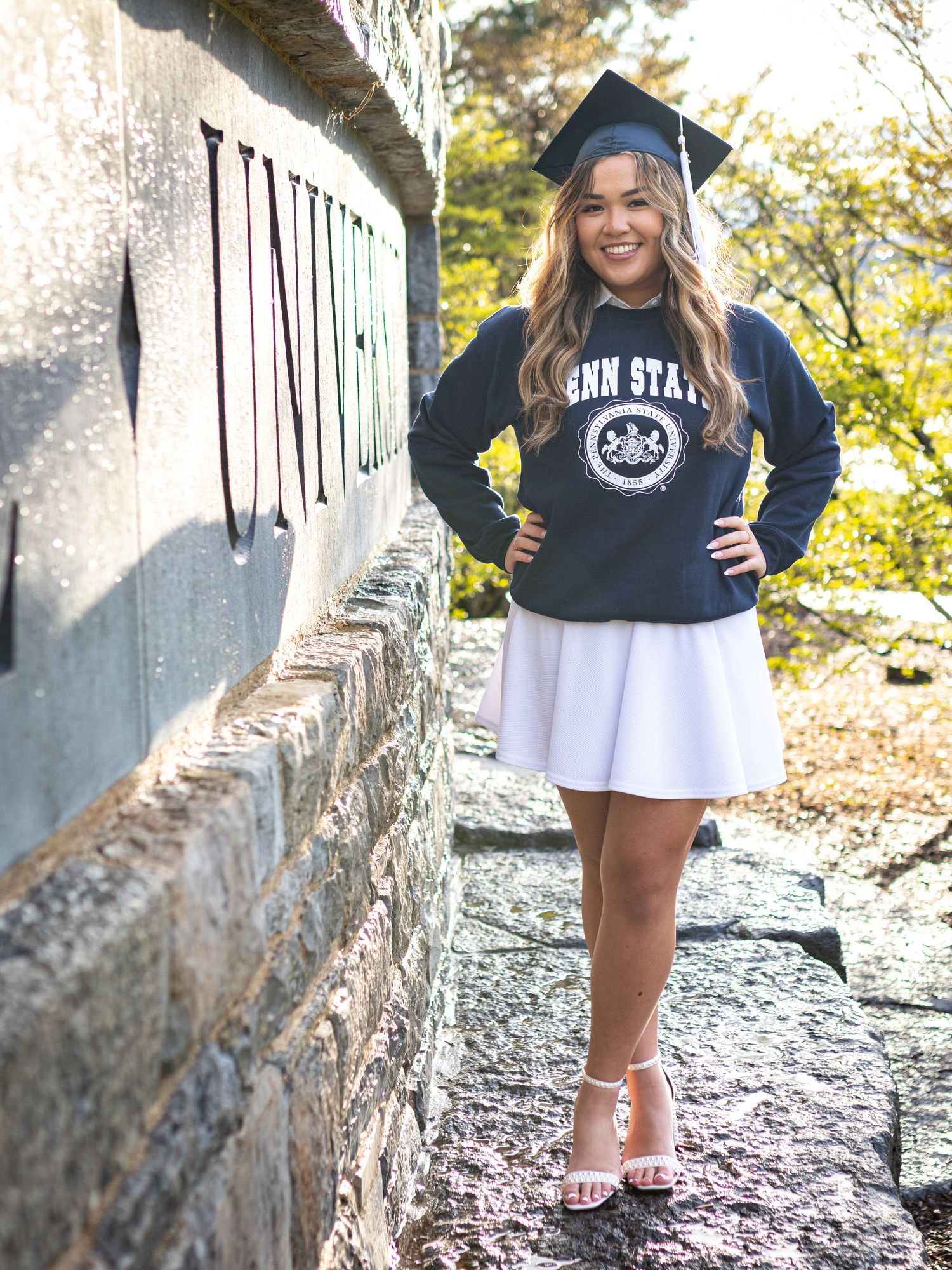 Penn State graduate in casual attire poses near stone wall outdoors.