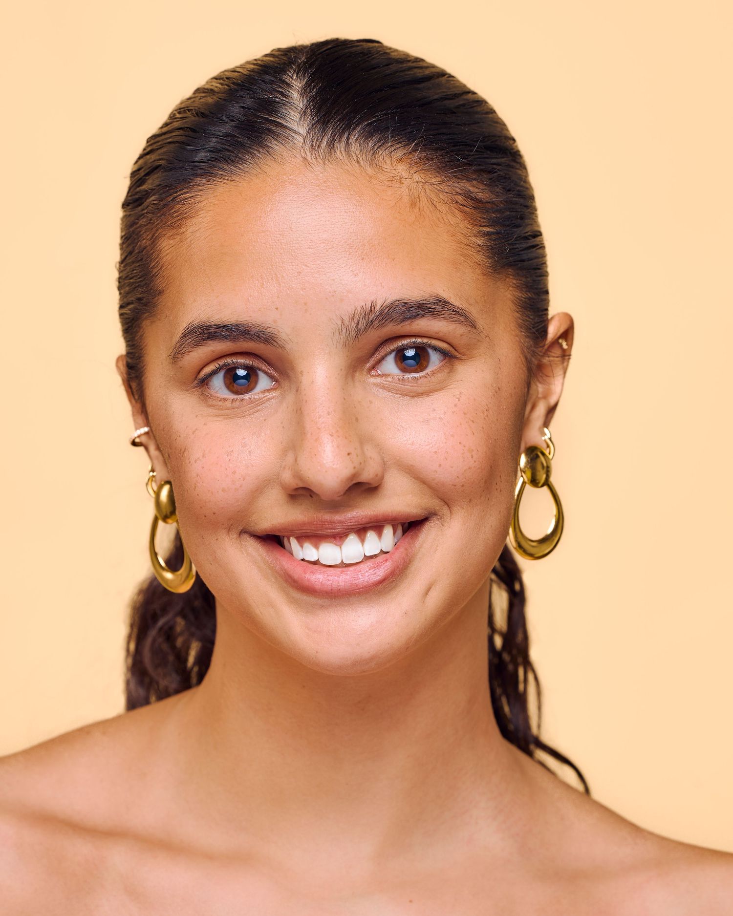 Woman with gold hoop earrings and natural makeup smiling against peach background in progression shots.