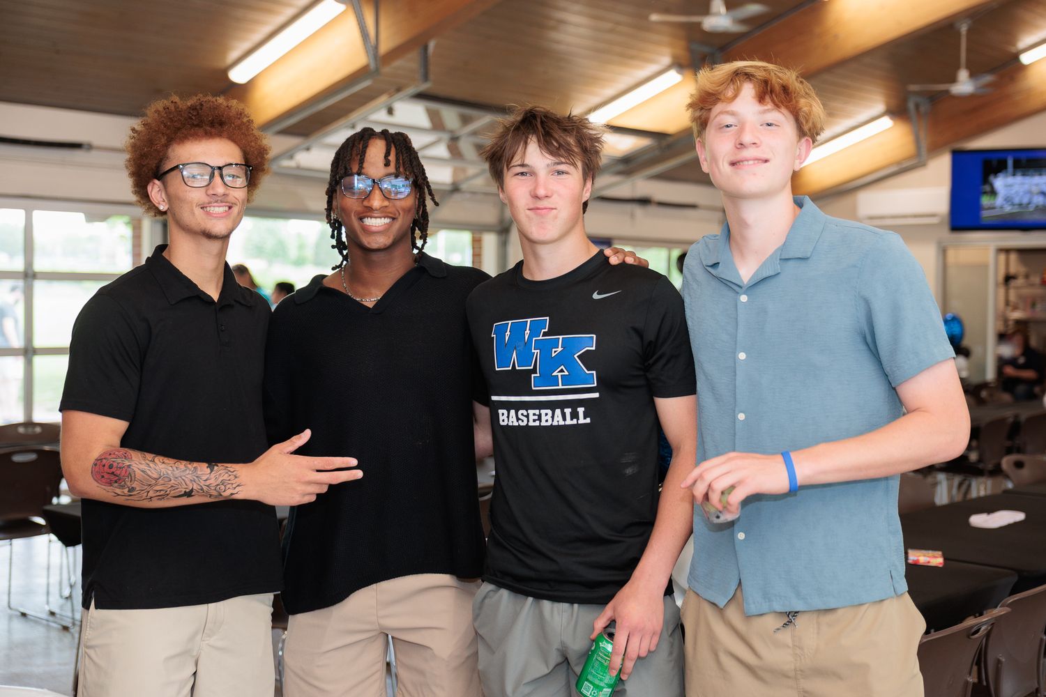 Four young men smiling and posing together indoors at a casual social gathering event.