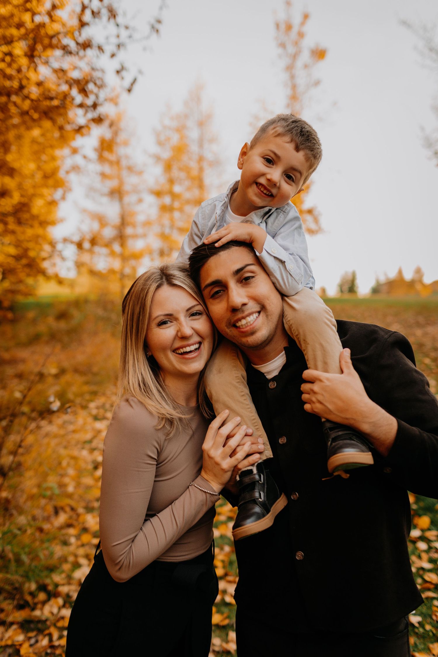 A joyful family poses together in an autumn setting with golden trees in the background.