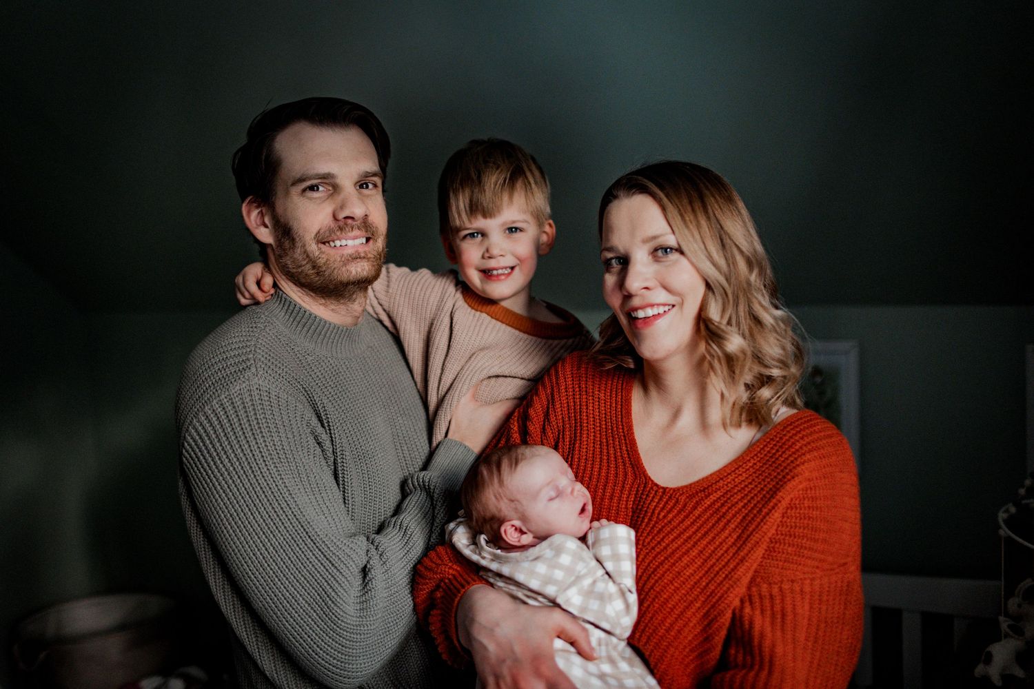 Cozy family portrait with small children in warm sweaters against dark background.