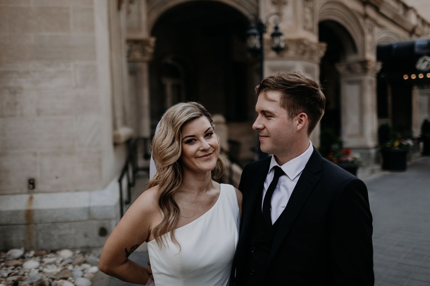 A couple poses together for wedding photos in an elegant stone archway setting.