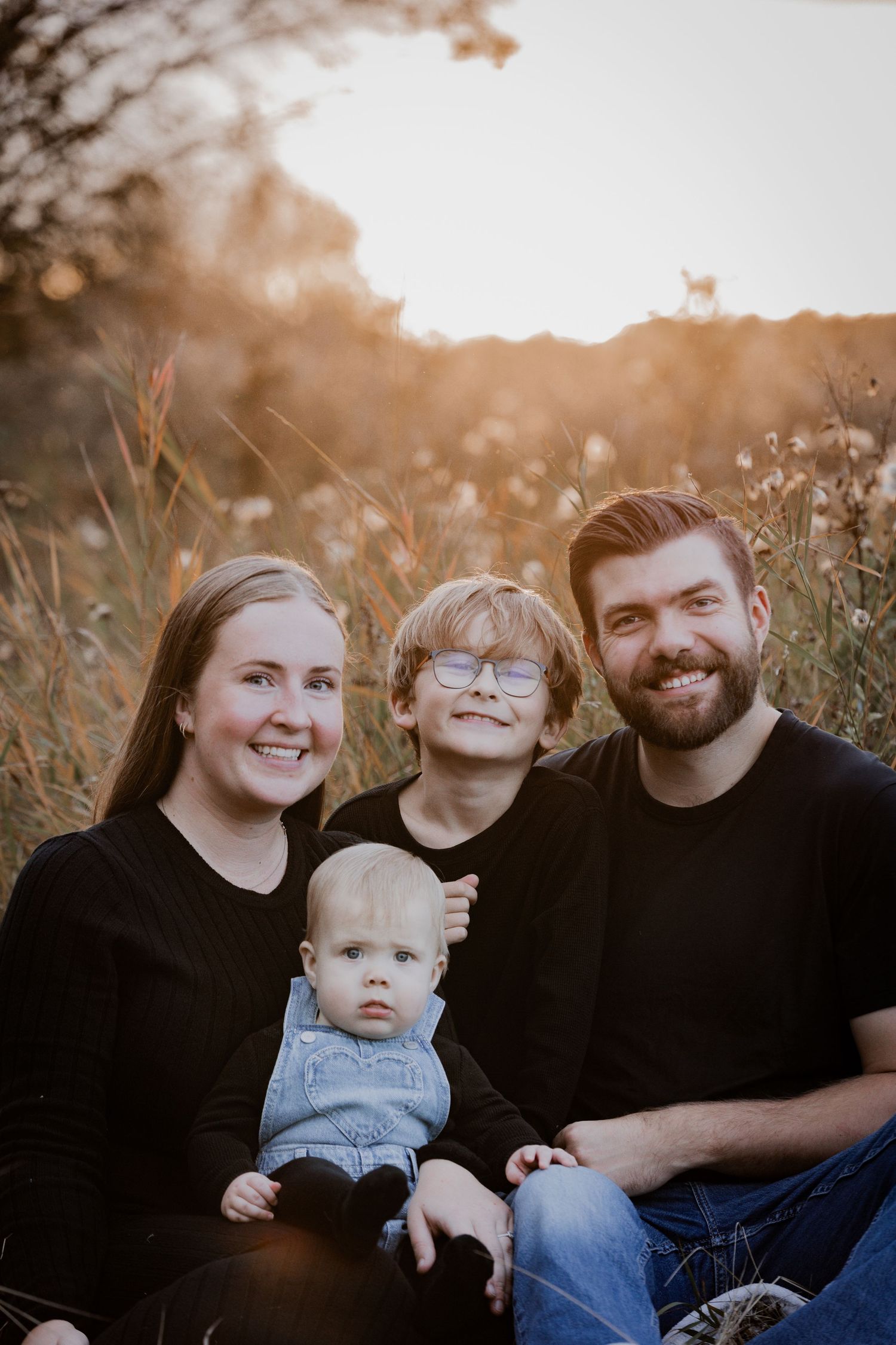A family of four sits together in a sunlit field during golden hour.