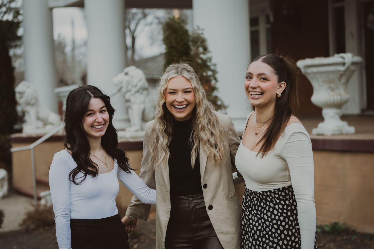 Three friends laughing together against an architectural backdrop with columns.