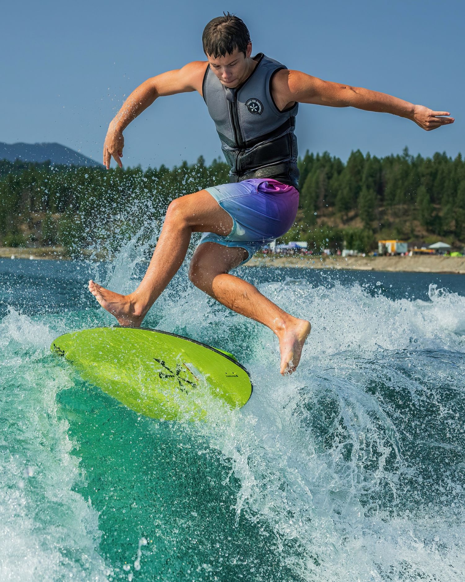 Wakeboarder performing aerial trick on green board with water splashing beneath.