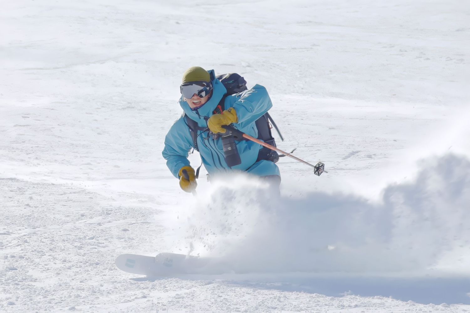 Skier spraying powder snow while carving down a steep slope.