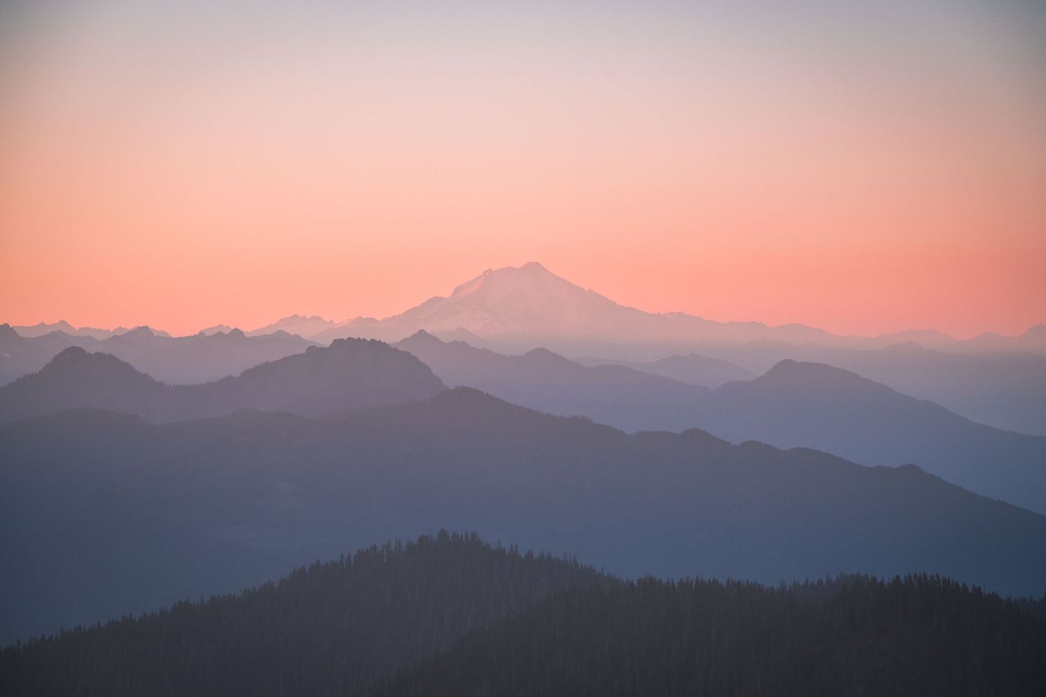 Silhouette of layered mountain ranges against a pink and purple sunset sky creating a misty ethereal landscape.