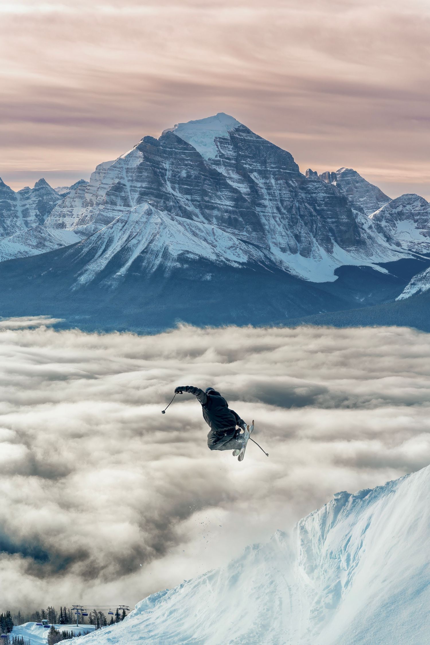 Skier performing jump above cloud layer with dramatic mountain peak backdrop.