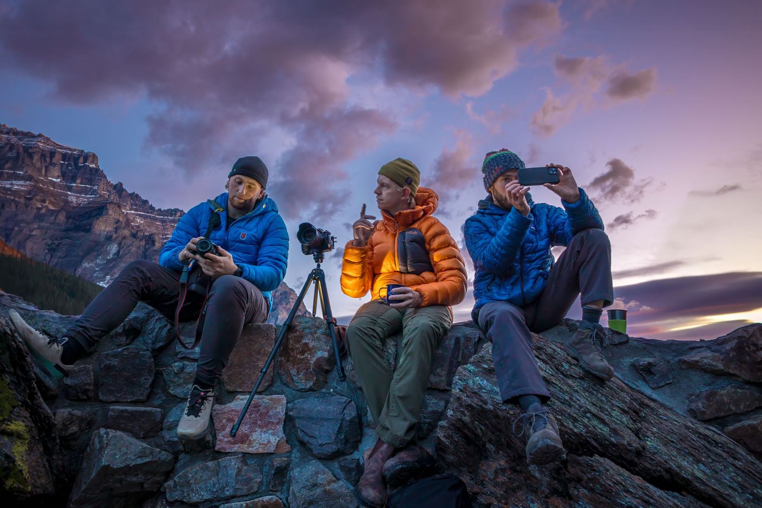 Photographers set up equipment on rocky outcrop during dramatic mountain sunset.