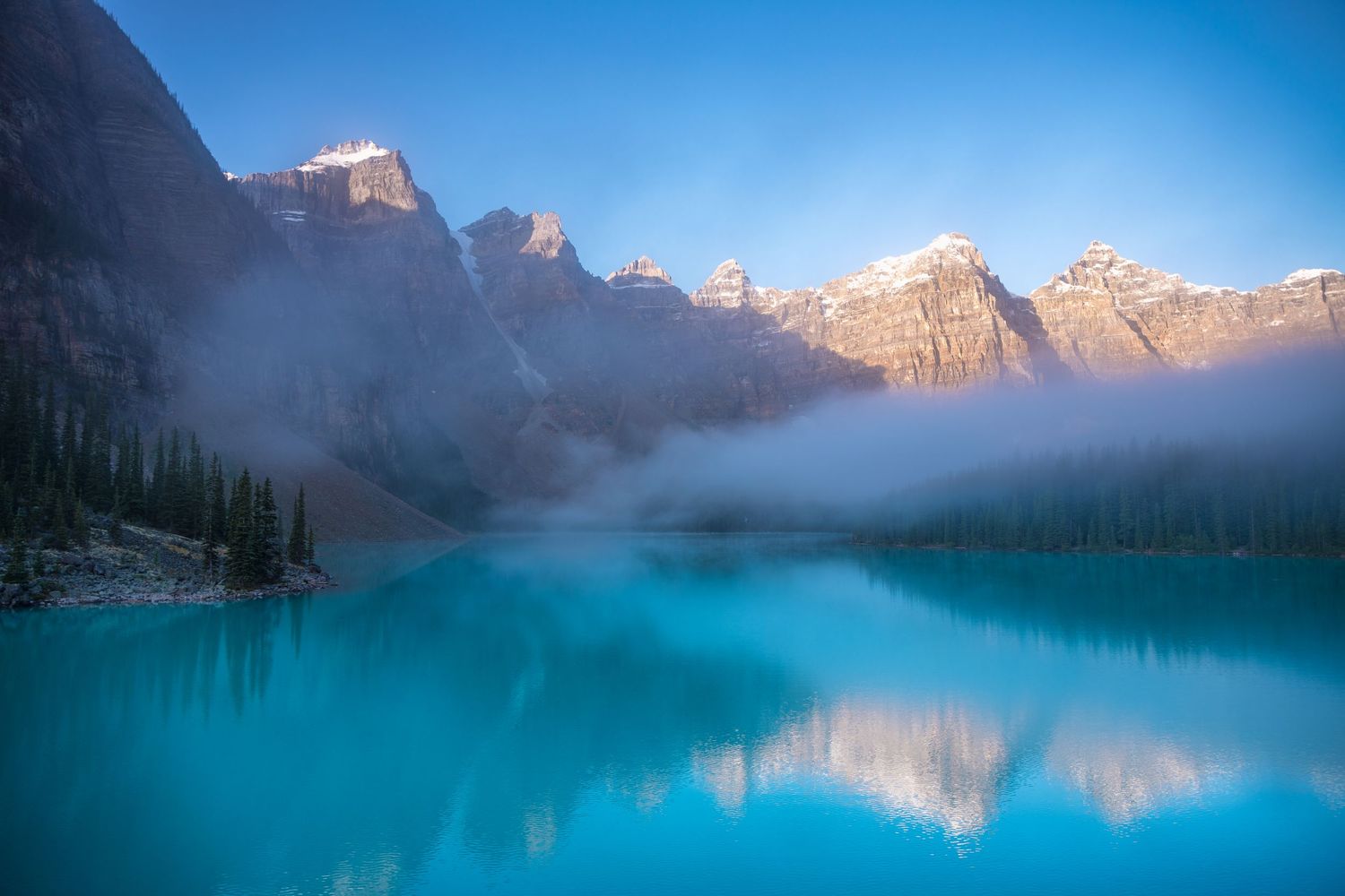 Misty sunrise over turquoise Moraine Lake with snow-capped peaks of Valley of Ten Peaks reflected in Banff National Park.