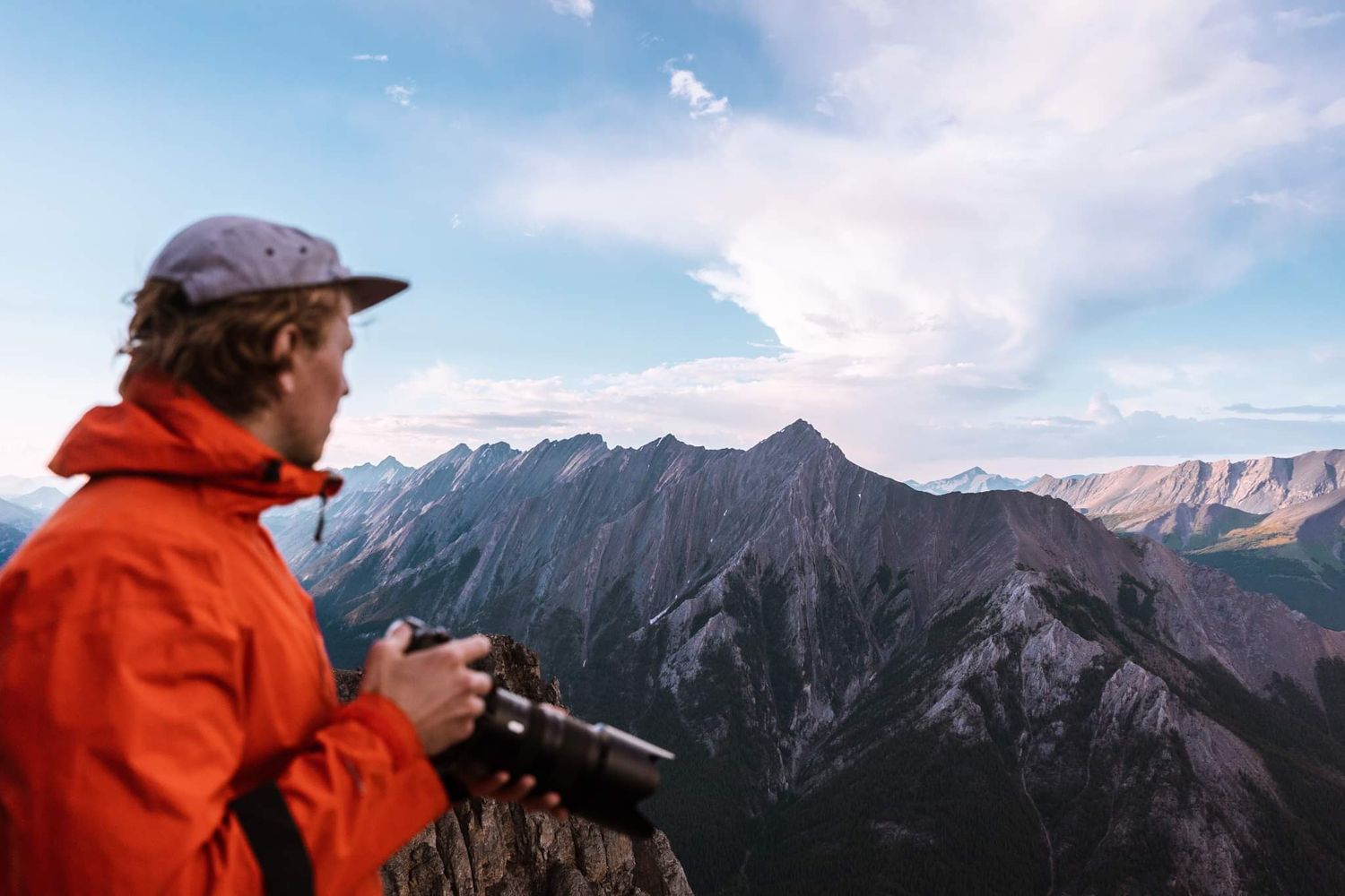 Photographer in orange jacket surveys dramatic mountain landscape with camera.