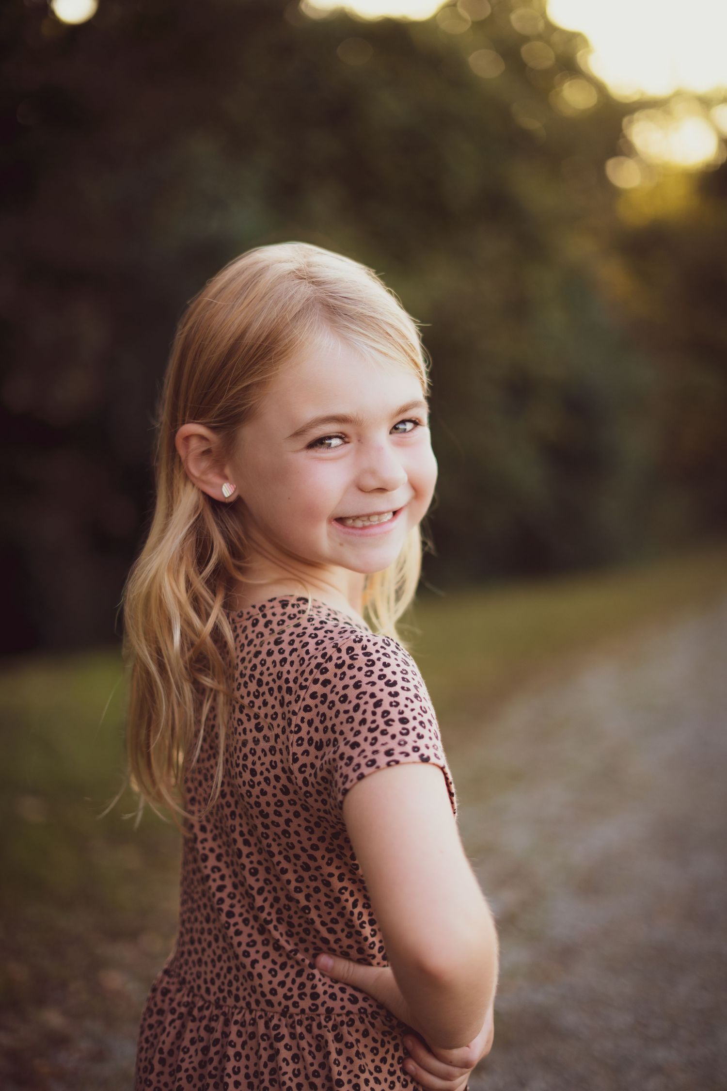 Young blonde girl in a pink leopard print dress smiling over her shoulder at golden hour.