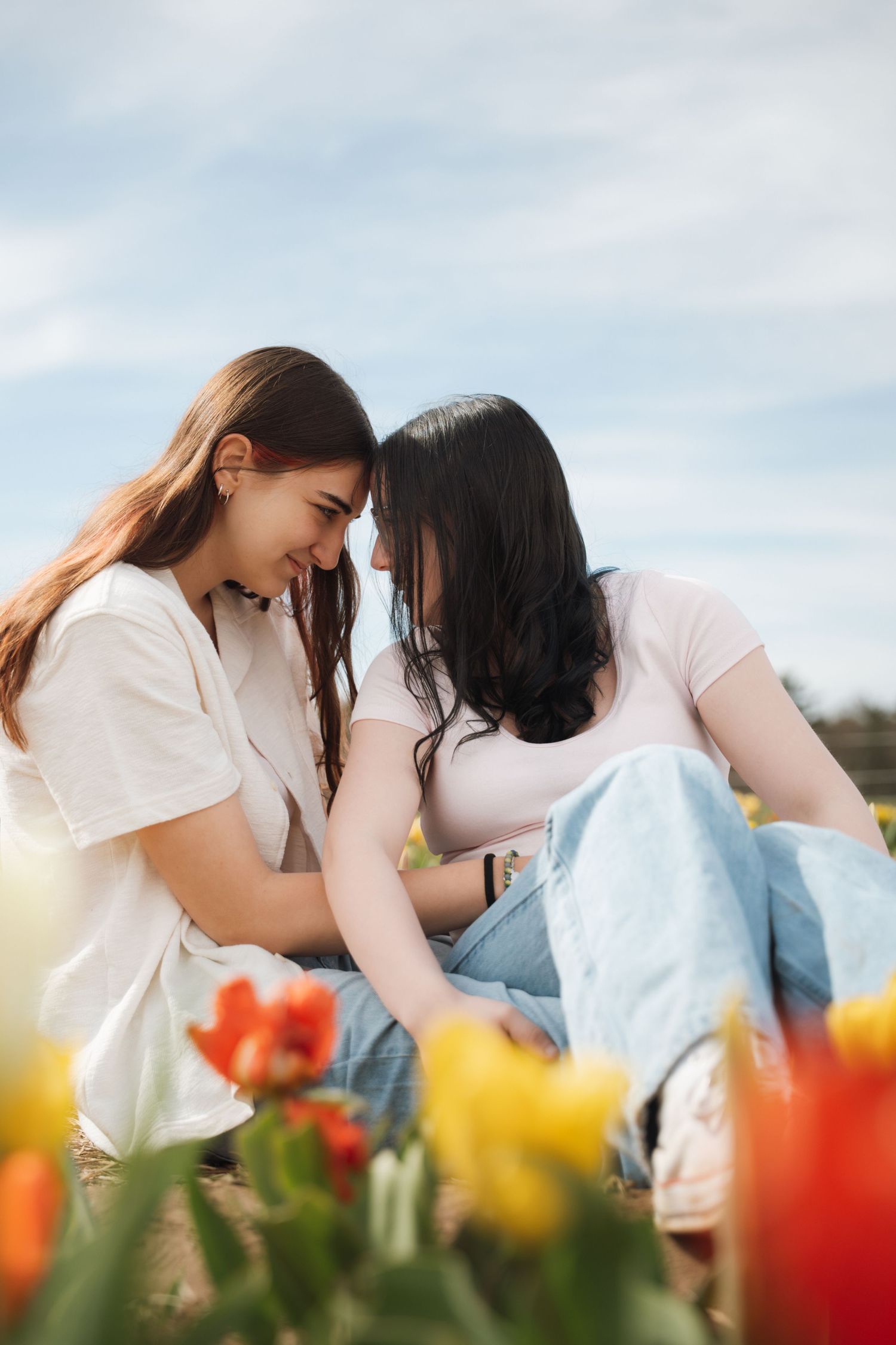 Two young women touching foreheads intimately while sitting among vibrant red and yellow tulips.