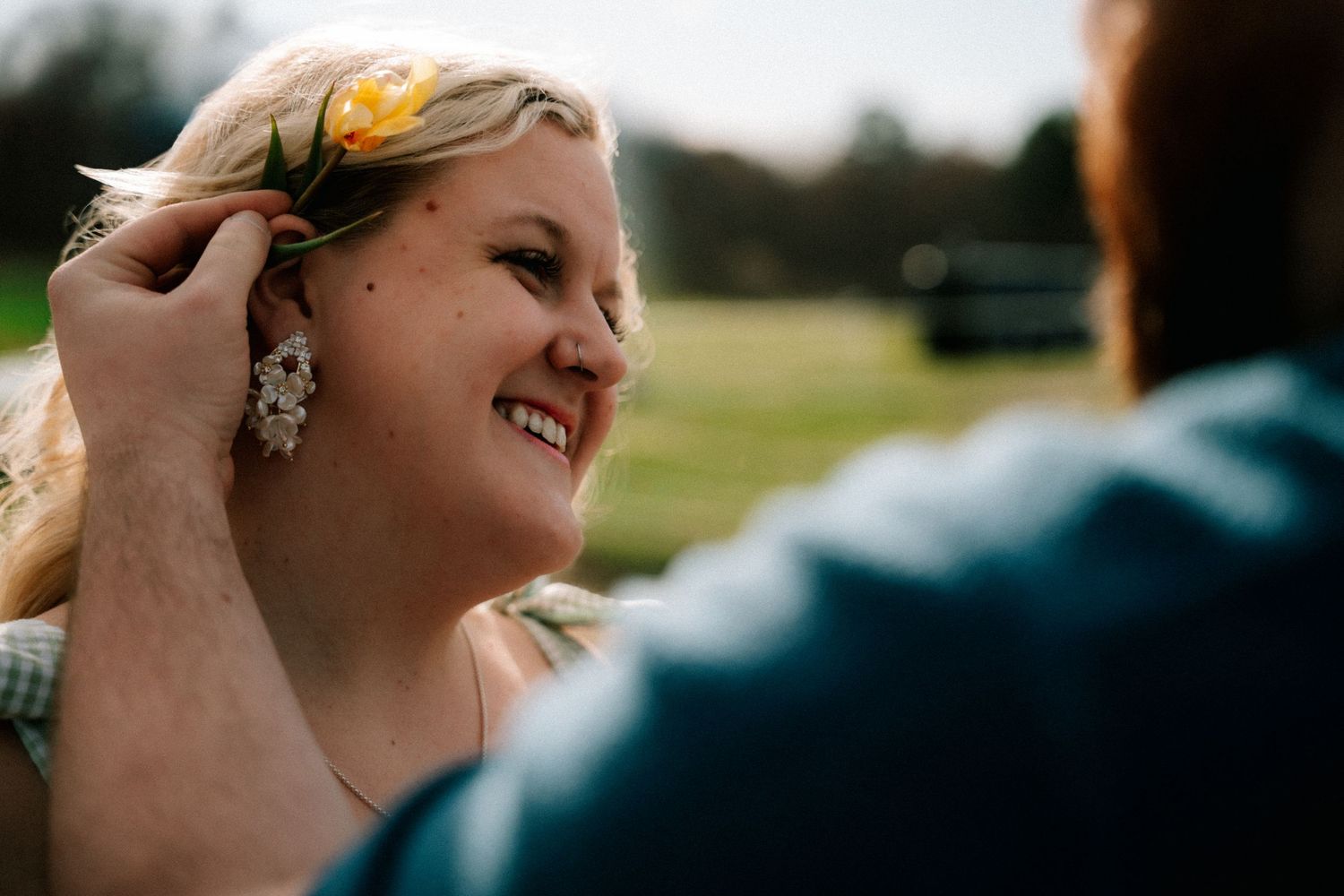 Smiling blonde woman having a yellow flower placed in her hair outdoors on a sunny day.
