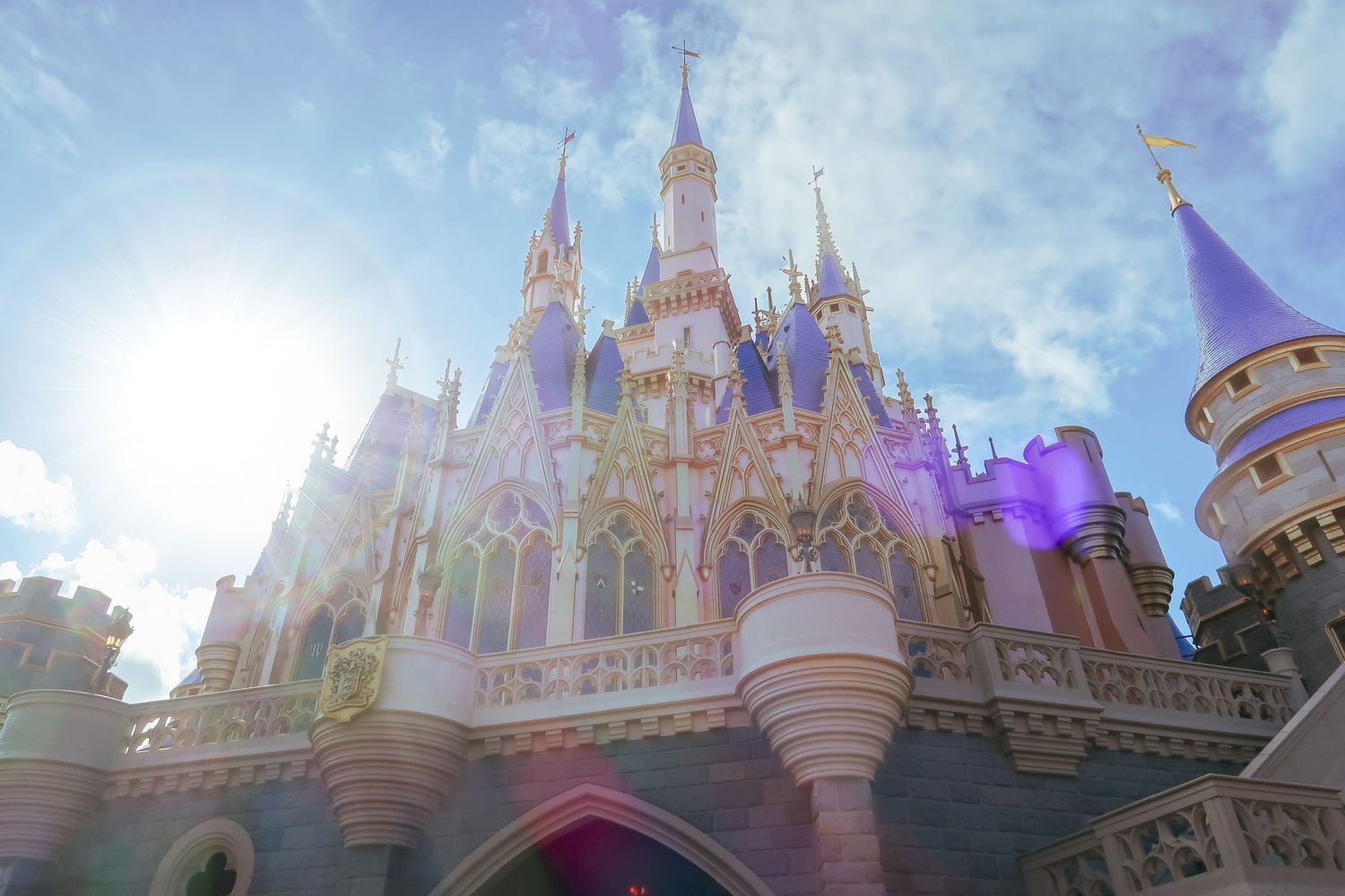 Cinderella Castle sparkles with pastel pink and purple hues under a bright sunlit sky.