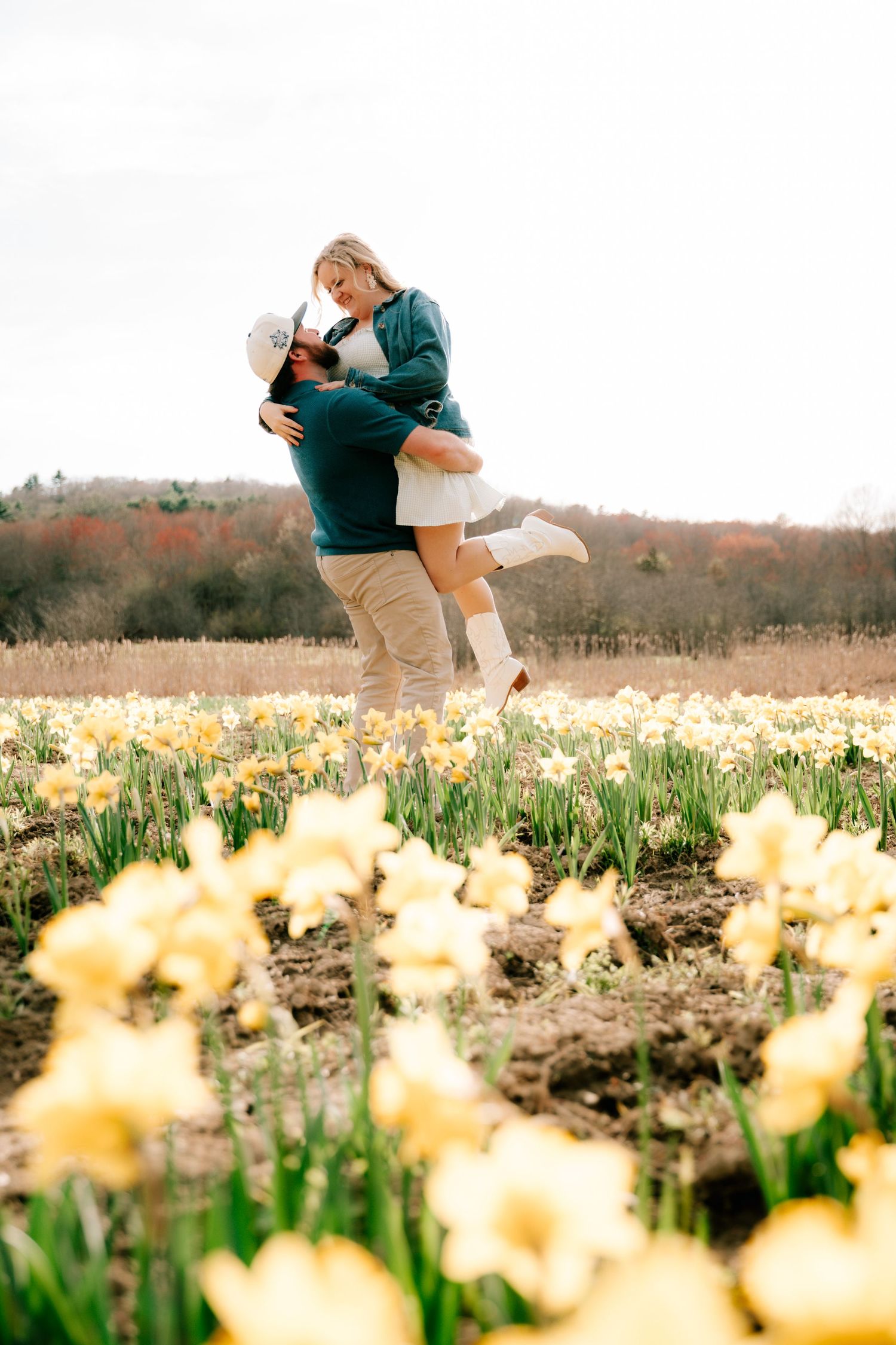 Man lifting woman in a romantic embrace surrounded by yellow daffodils in a spring field.