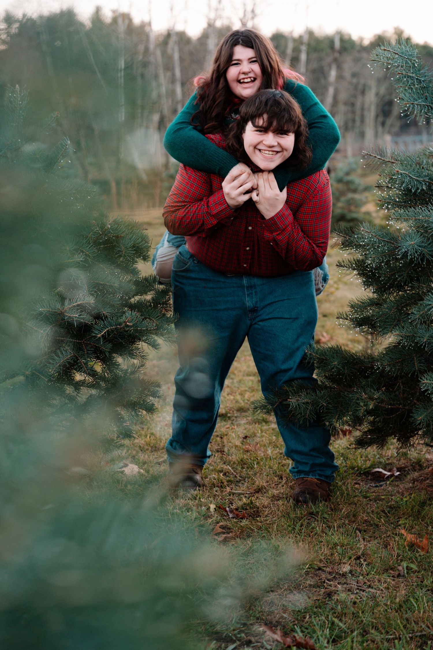 Couple laughing with piggyback ride at Christmas tree farm.