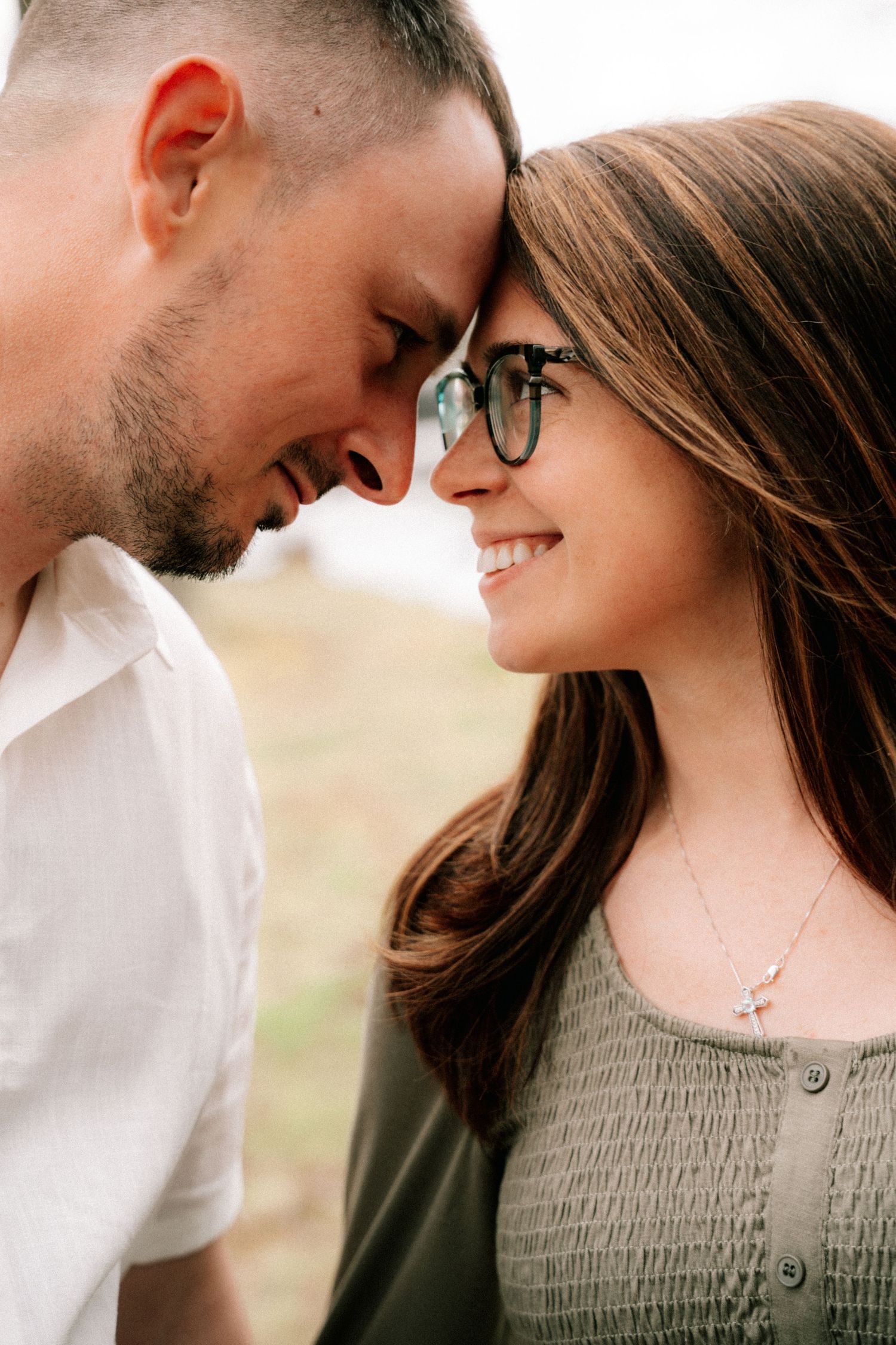 Romantic couple touching foreheads and smiling closely together outdoors on a sunny day.