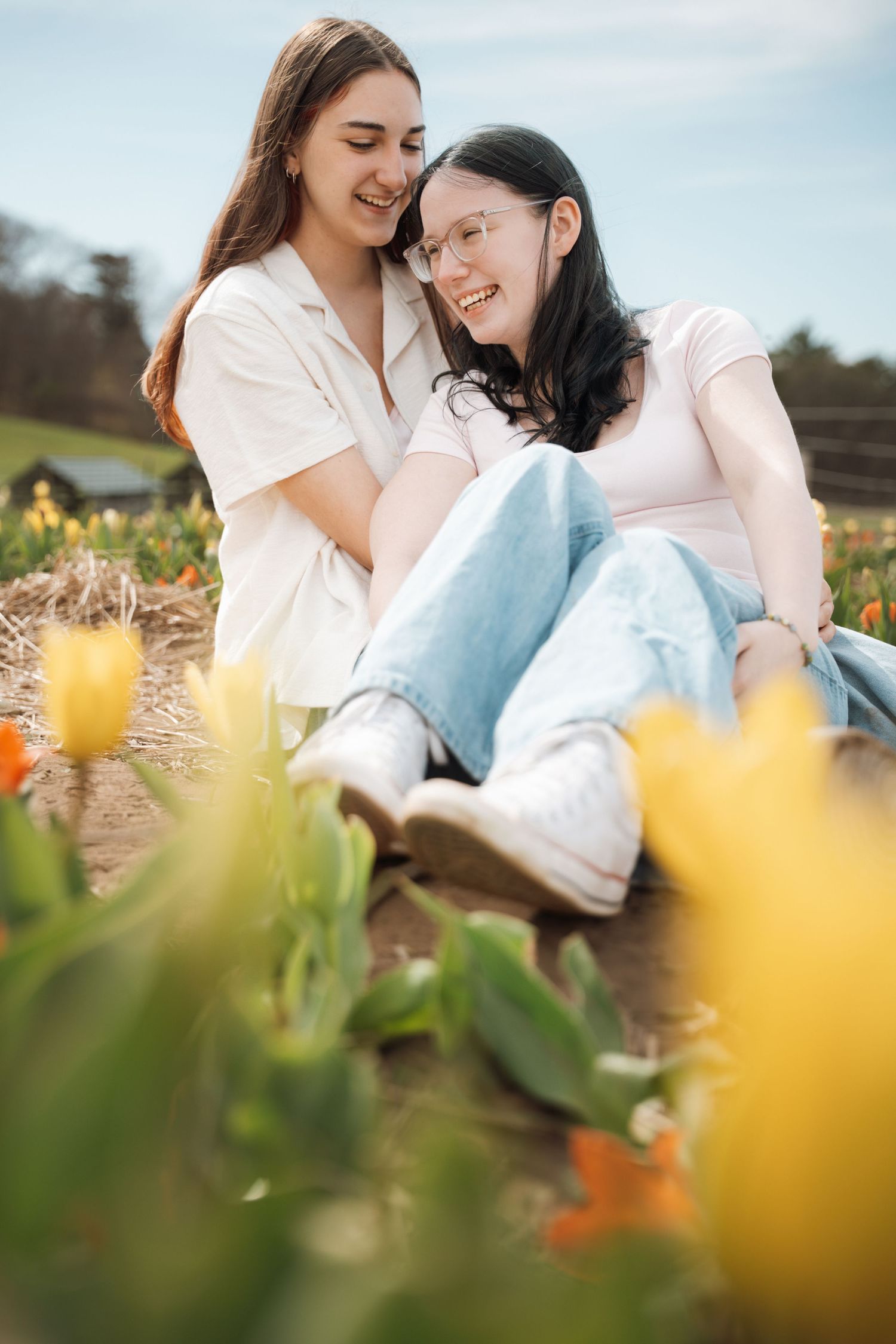 Two young women sitting together smiling in a colorful tulip field on a sunny day.